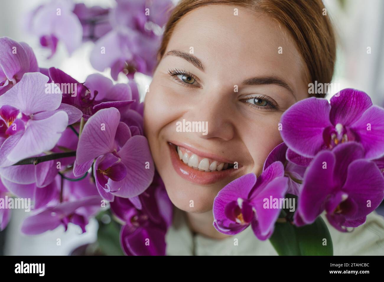 Visage de femme fleuriste souriante dans les fleurs d'orchidée, gros plan Banque D'Images