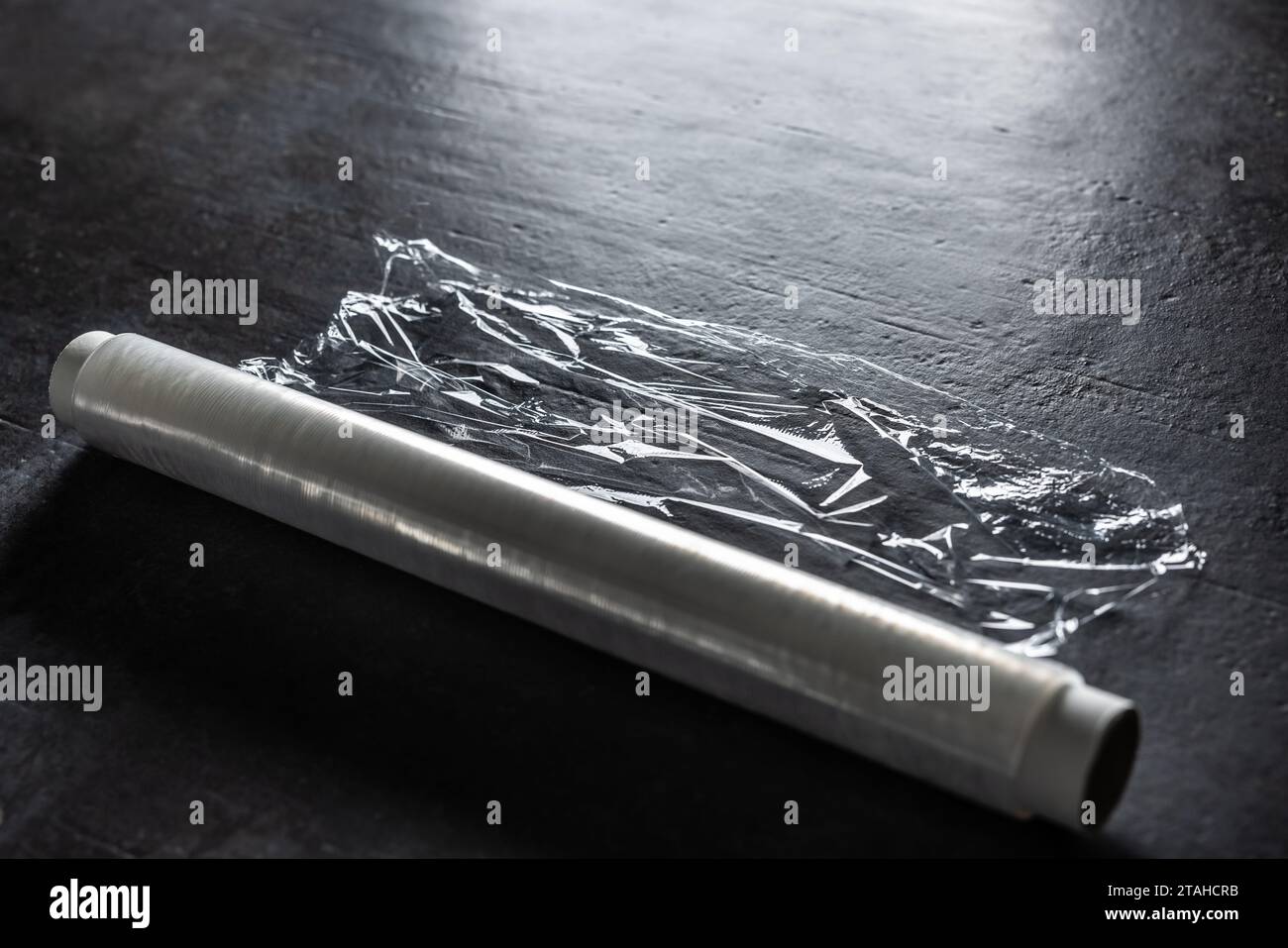Rouleau de film étirable en plastique d'emballage blanc sur la table en béton foncé. Banque D'Images