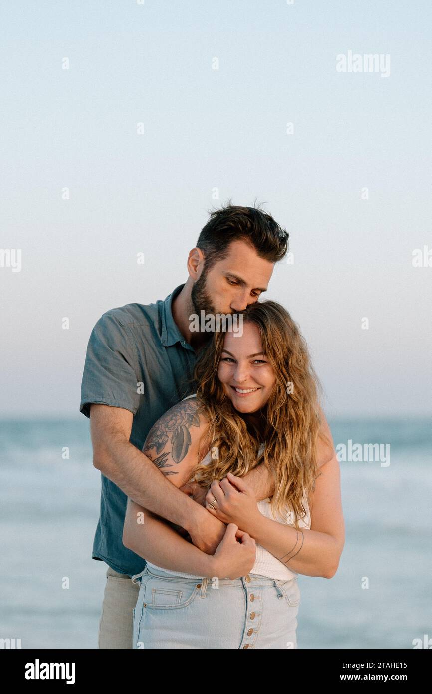 Homme embrassant sa femme sur le dessus de la tête à la plage Banque D'Images