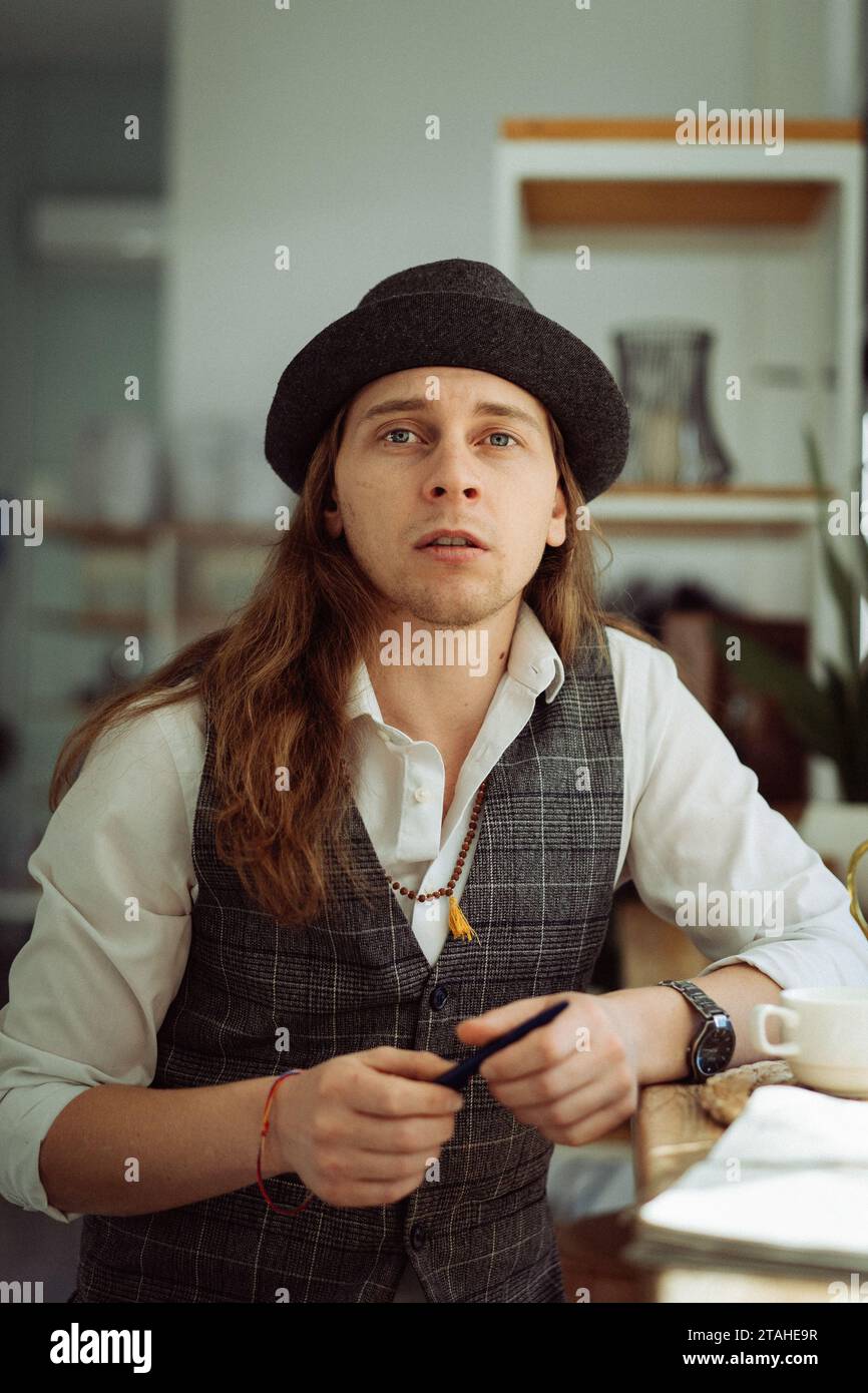 Jeune homme caucasien aux longs cheveux blonds dans un café. Banque D'Images