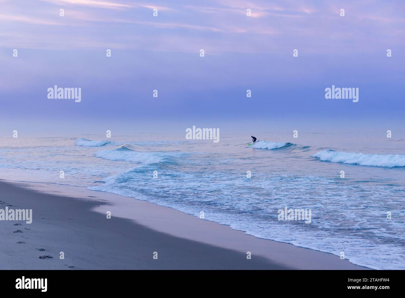 Un surfeur aux silhouettes attrape une vague sur Cape Cod au coucher du soleil Banque D'Images