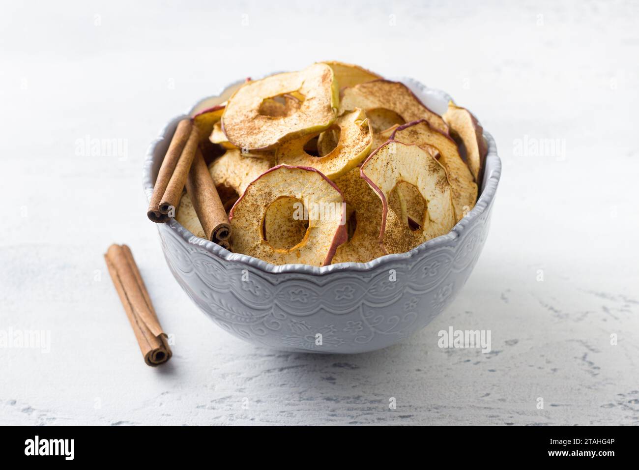 Pommes séchées maison à la cannelle, chips de pomme dans un bol avec des bâtons de cannelle sur un fond gris clair. Délicieux en-cas sain Banque D'Images