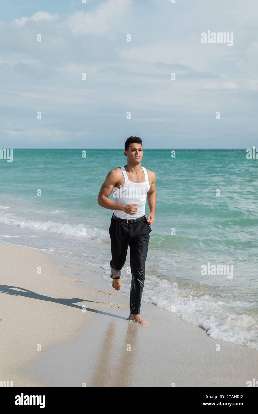 Jeune homme cubain musclé courant sur le sable près de l'eau de l'océan de Miami South Beach, Floride Banque D'Images