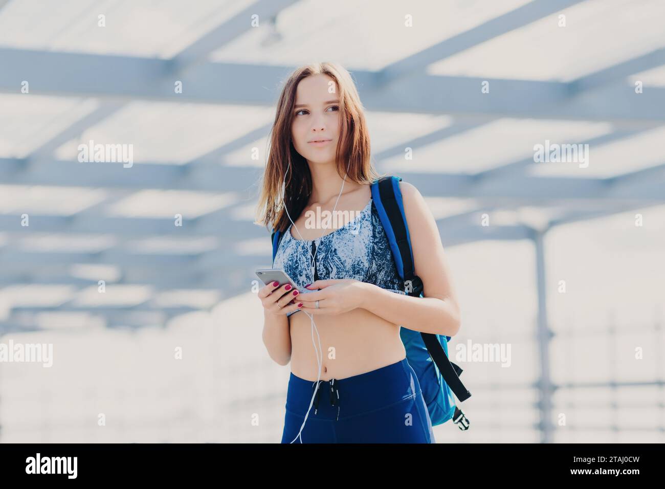 Femme athlétique avec téléphone et sac à dos marchant à l'extérieur Banque D'Images