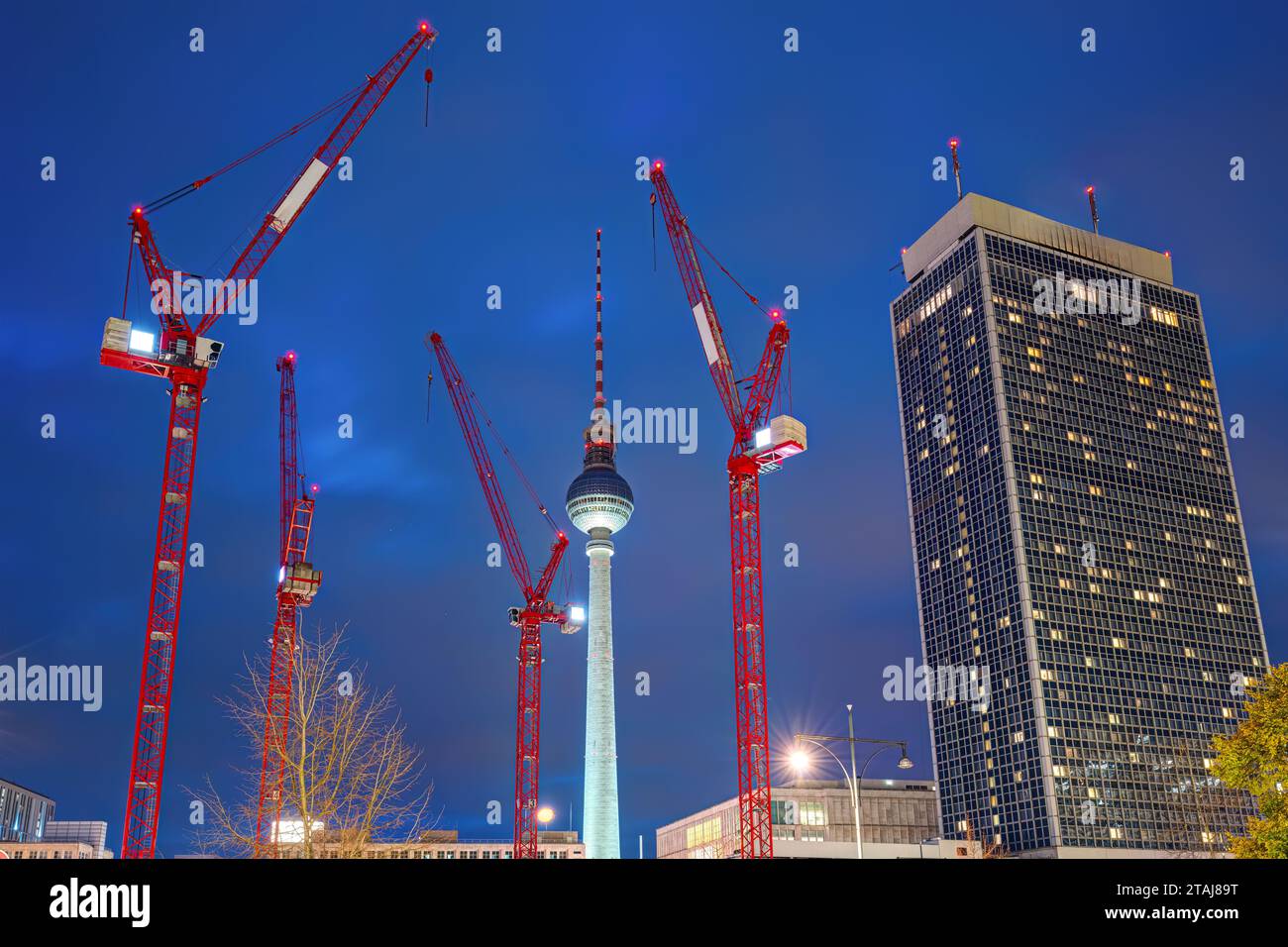 La célèbre tour de télévision de Berlin la nuit avec un gratte-ciel et quatre grues de construction rouges Banque D'Images