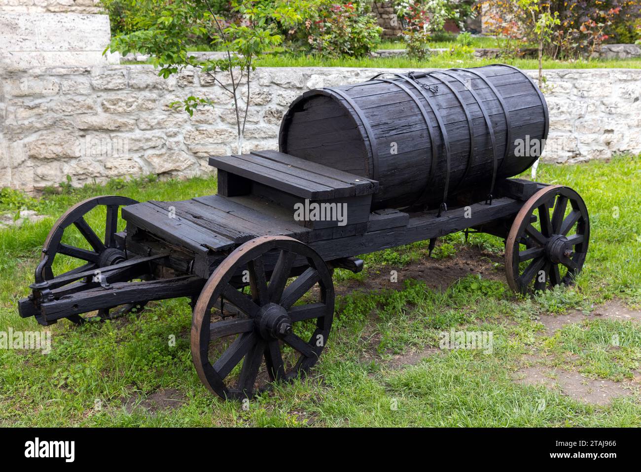 Vieux wagon en bois avec baril se tient sur l'herbe verte près du mur de pierre rural Banque D'Images