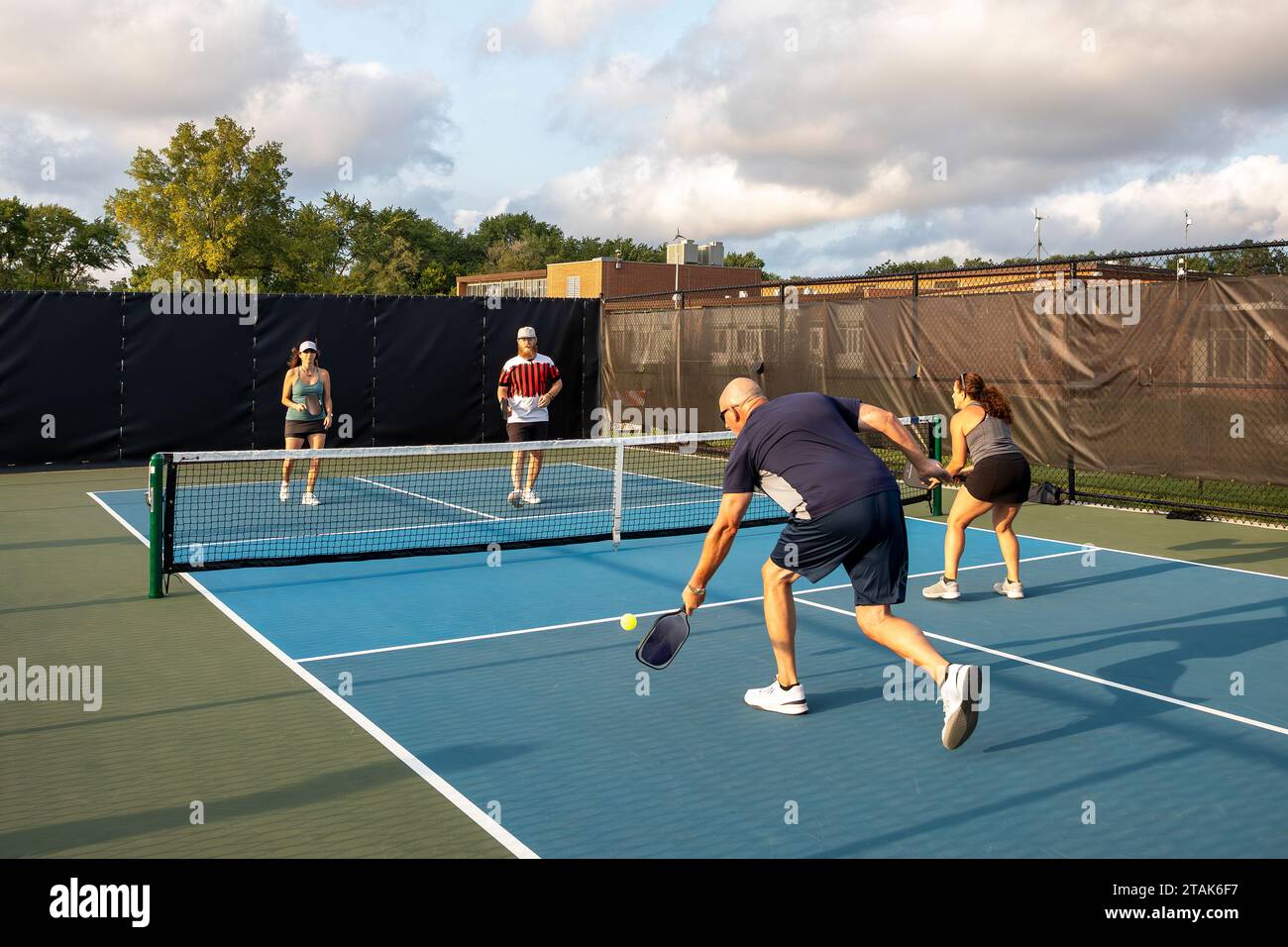 Quatre joueurs de pickleball se rassemblent les uns contre les autres alors que l'un tente de retourner un tir tandis que ses adversaires marchent vers la zone de non-volley. Banque D'Images