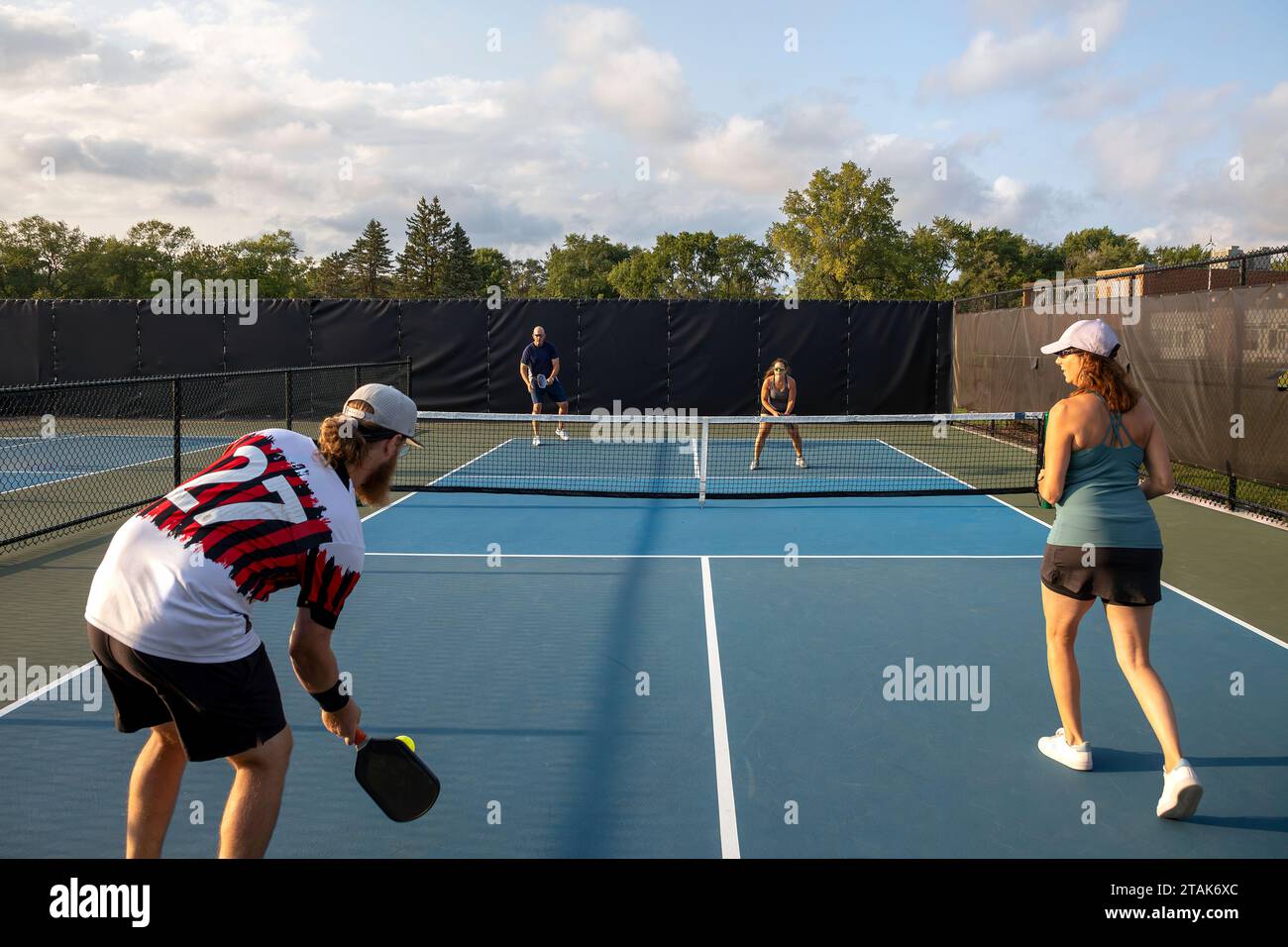 Quatre joueurs de pickleball se rassemblent les uns contre les autres avec deux à la ligne de base prêts à déposer une balle dans la zone de non-volley de leurs adversaires. Banque D'Images