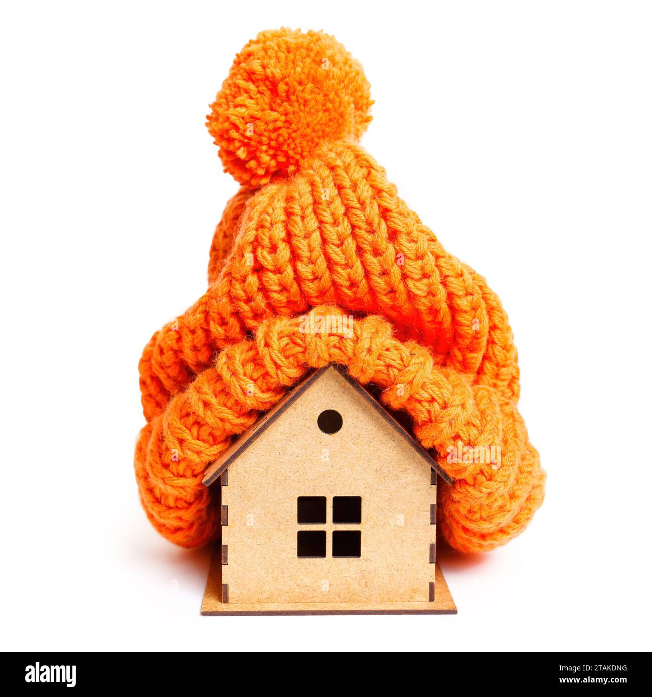 Chapeau tricoté orange avec un pompon ornant une maison en bois jouet isolé sur blanc. Chaleur et confort du confort de la maison d'hiver. Banque D'Images