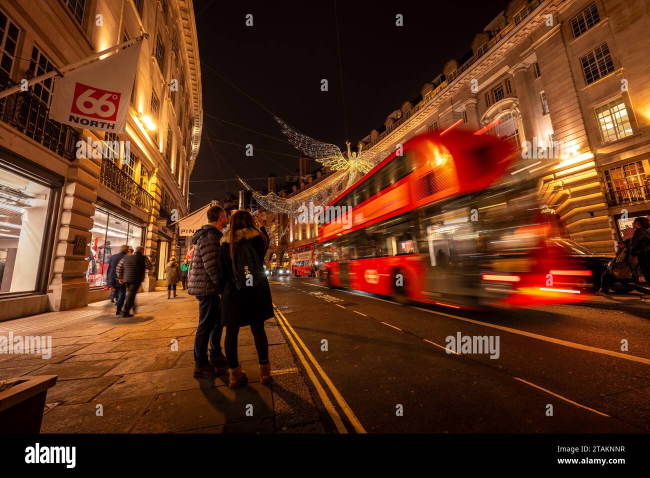 Londres, Royaume-Uni - novembre 20 2023 : Regent Street avec des lumières de Noël au-dessus. Les gens prennent une photo alors qu'un bus rouge londonien passe avec un flou de mouvement. Banque D'Images