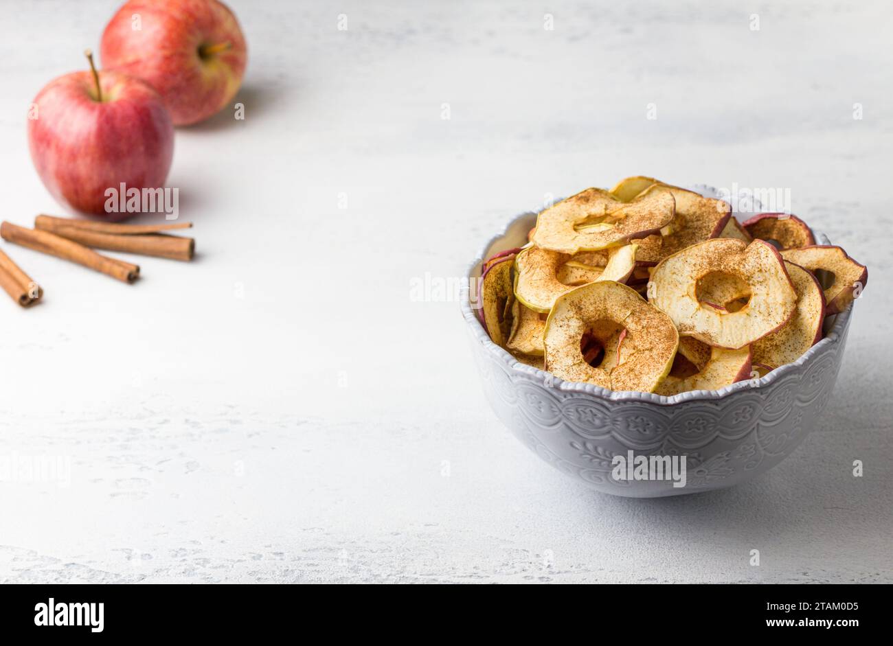 Pommes séchées maison à la cannelle, chips de pomme dans un bol avec des bâtons de cannelle sur un fond gris clair. Délicieux en-cas sain Banque D'Images