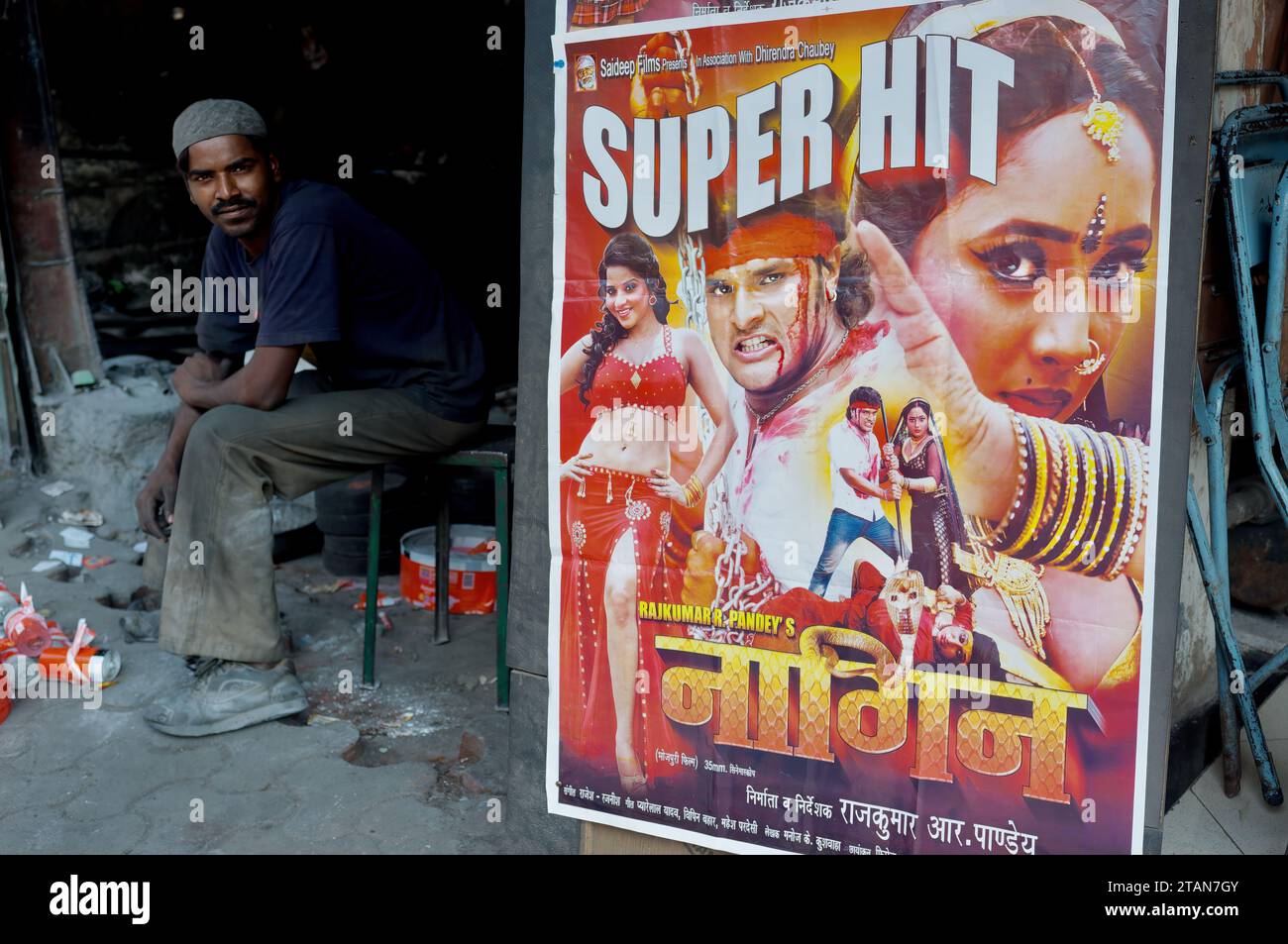 Un Indien est assis dans un atelier à côté d'une publicité pour le film en langue Bhojpuri 'Nagin' (Snake Woman, Venomous Woman) ; Mumbai, Inde Banque D'Images