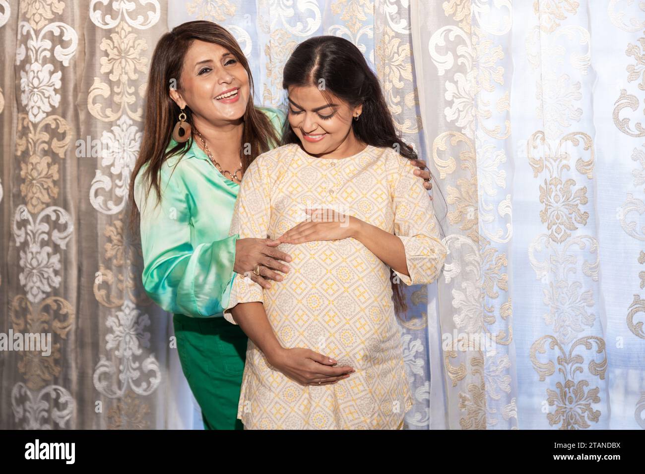 Femme indienne enceinte avec sa mère touchant le gros ventre près de la fenêtre à la maison. concept de personnes et d'attentes Banque D'Images