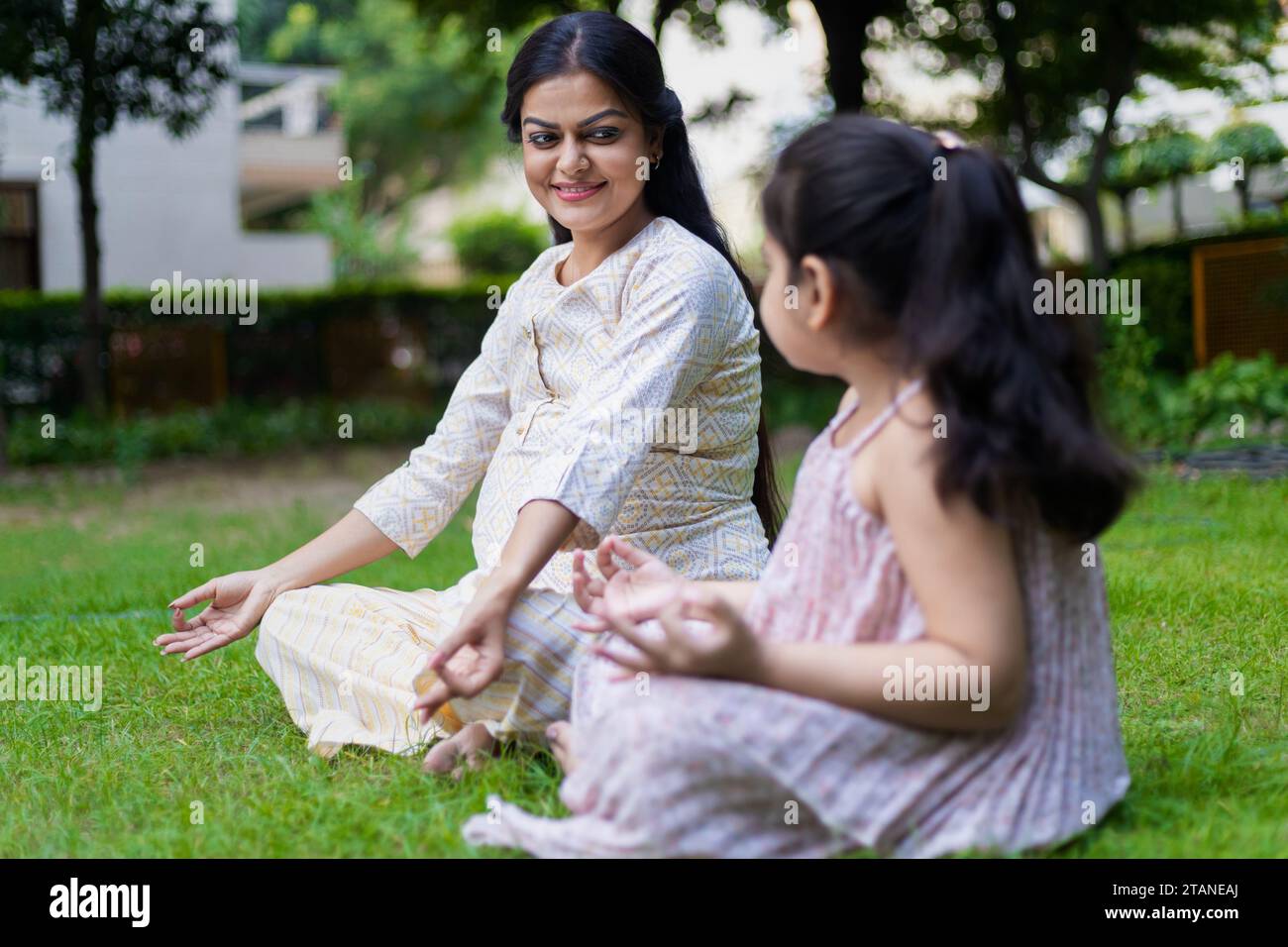 Belle jeune femme indienne enseignant sa jolie fille yoga lotus position dans le parc ou le jardin. Banque D'Images