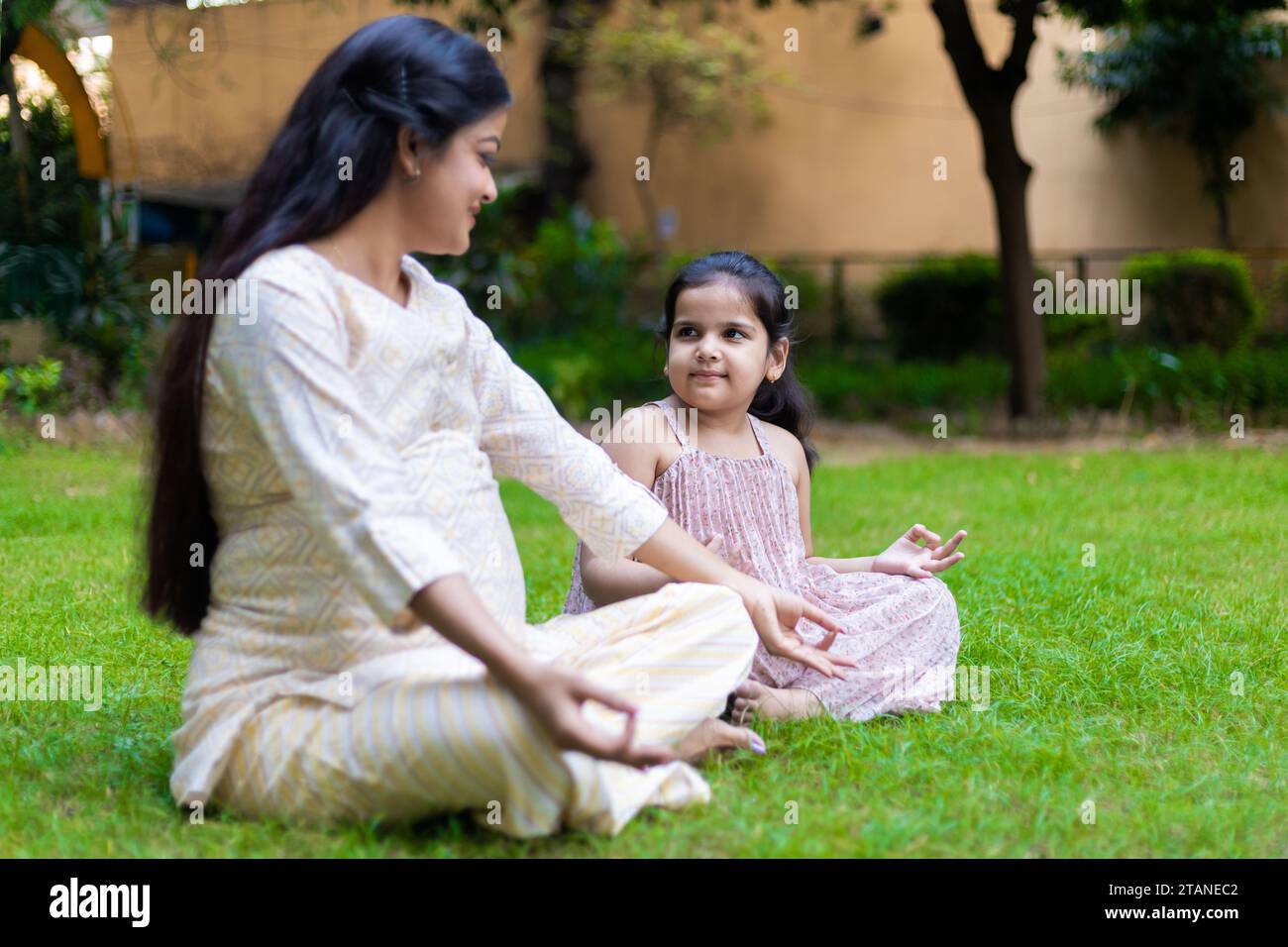 Belle jeune femme indienne enseignant sa jolie fille yoga lotus position dans le parc ou le jardin. Banque D'Images