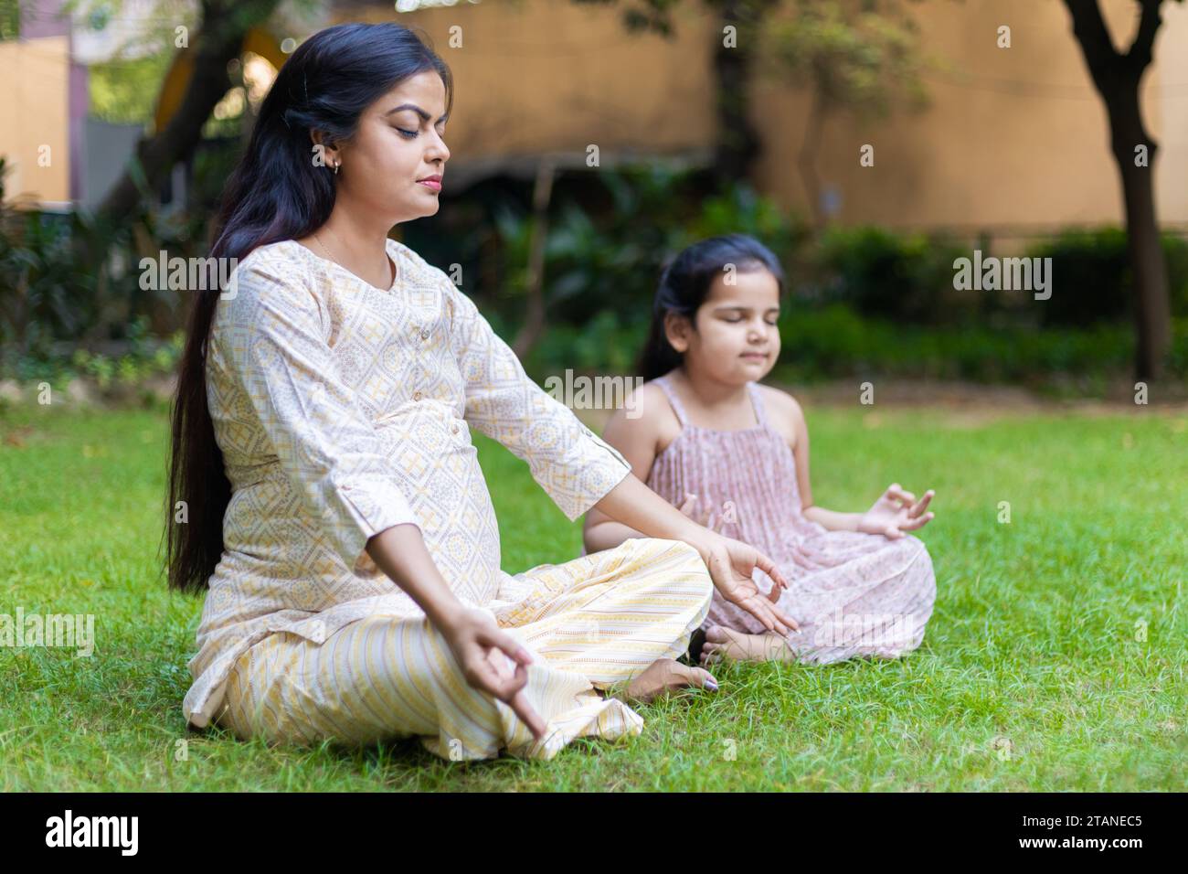 Belle jeune femme indienne enseignant sa jolie fille yoga lotus position dans le parc ou le jardin. Banque D'Images