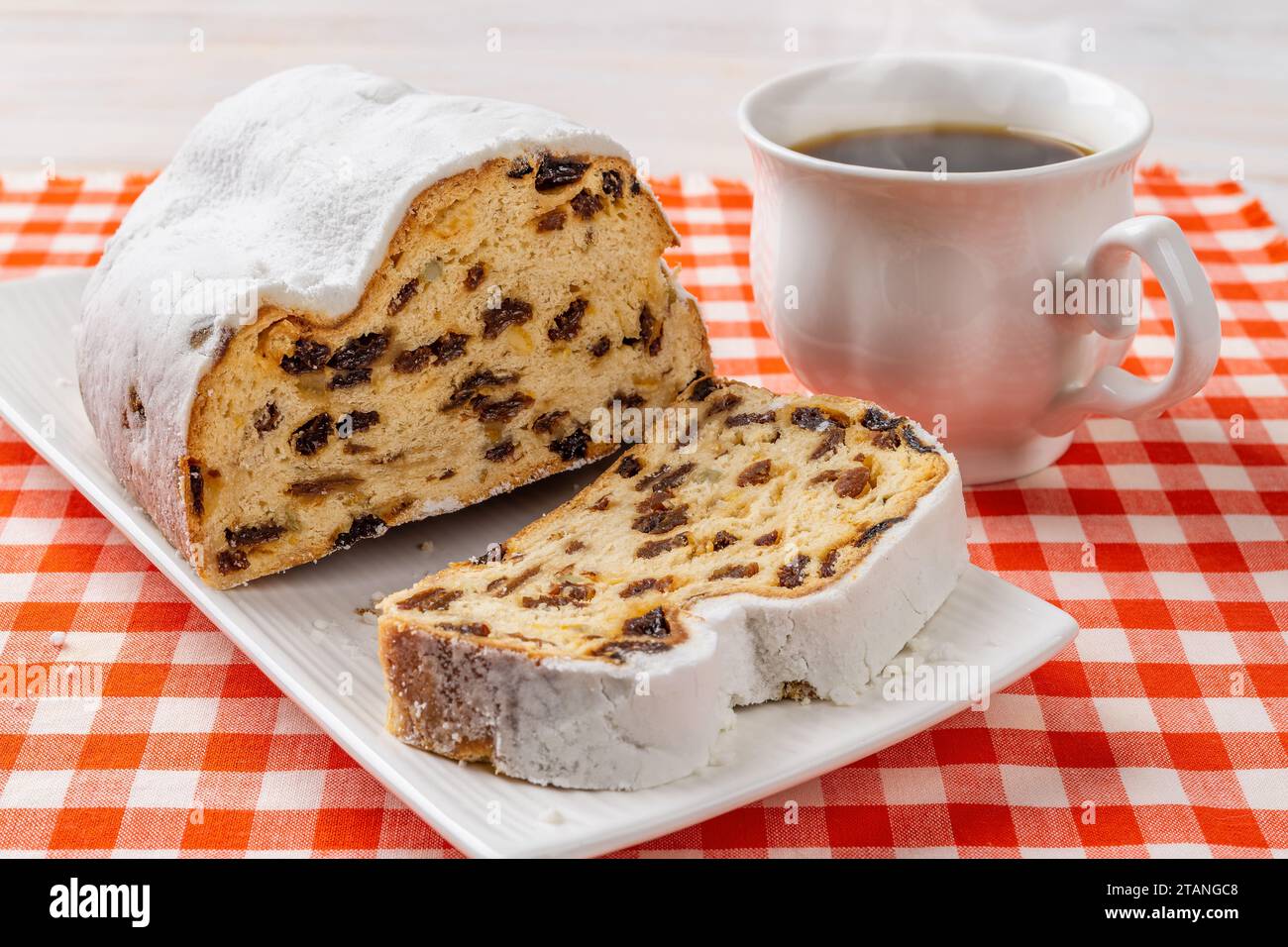 Tranche sucrée stollé et tasse de thé chaud. Tranche de pain de Noël allemand traditionnel sur une assiette et une tasse de café sur fond rouge à carreaux. Banque D'Images