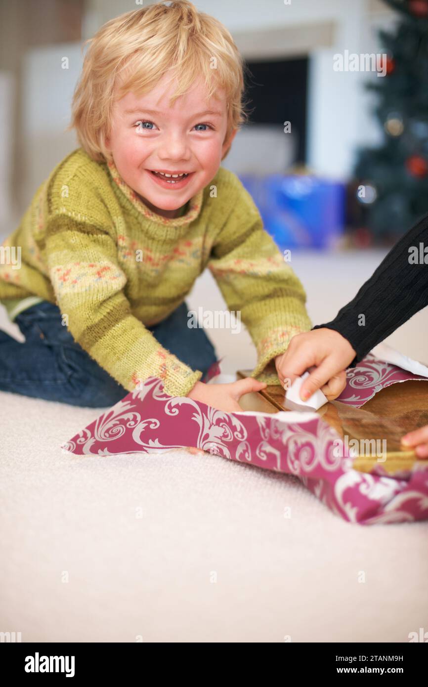 Portrait, garçon et ouverture cadeaux de noël pour les vacances, heureux et excité pour le cadeau. Célébration, sourire et maison familiale avec décorations, tradition Banque D'Images