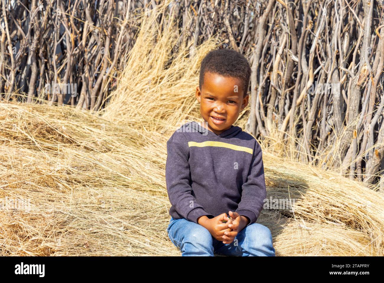 village africain, enfant assis sur l'herbe de chaume dans la cour près de la clôture Banque D'Images