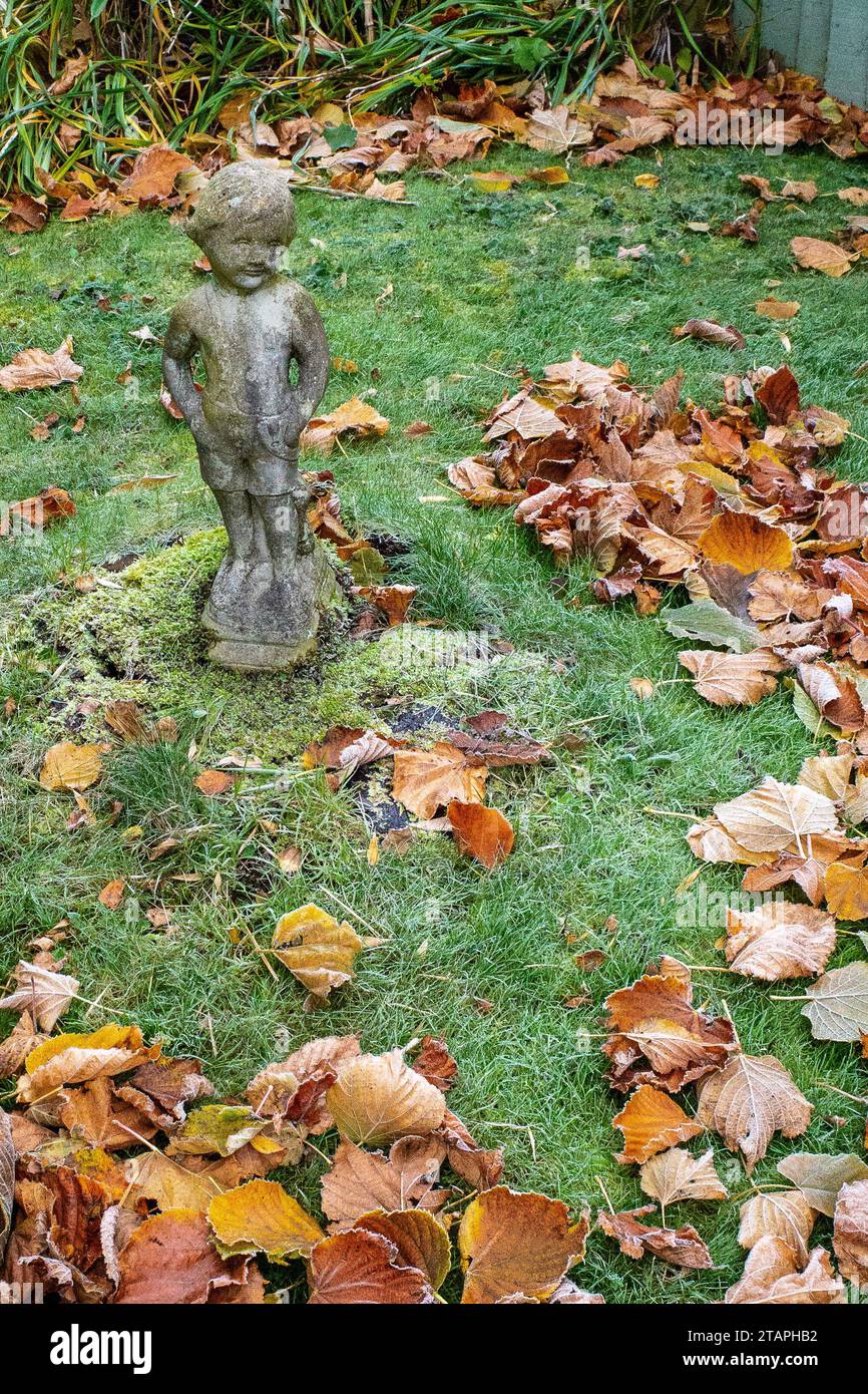 Statue de cupidon en pierre patinée dans un jardin britannique d'automne entouré de feuilles dorées. Matin glacial en hiver. Concept Death. Désolation. Banque D'Images