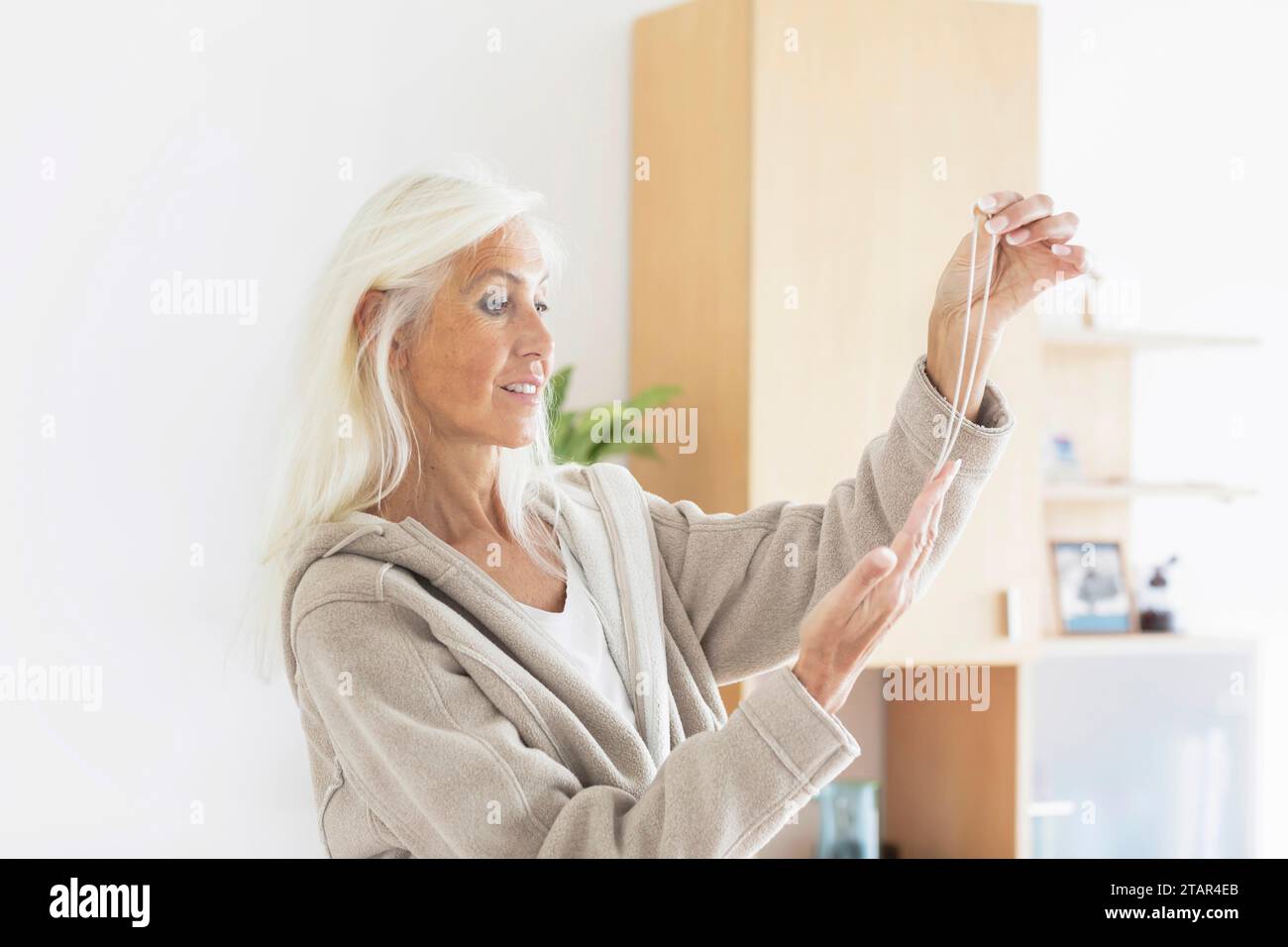 Femme âgée aux cheveux longs regardant un collier à la maison Banque D'Images