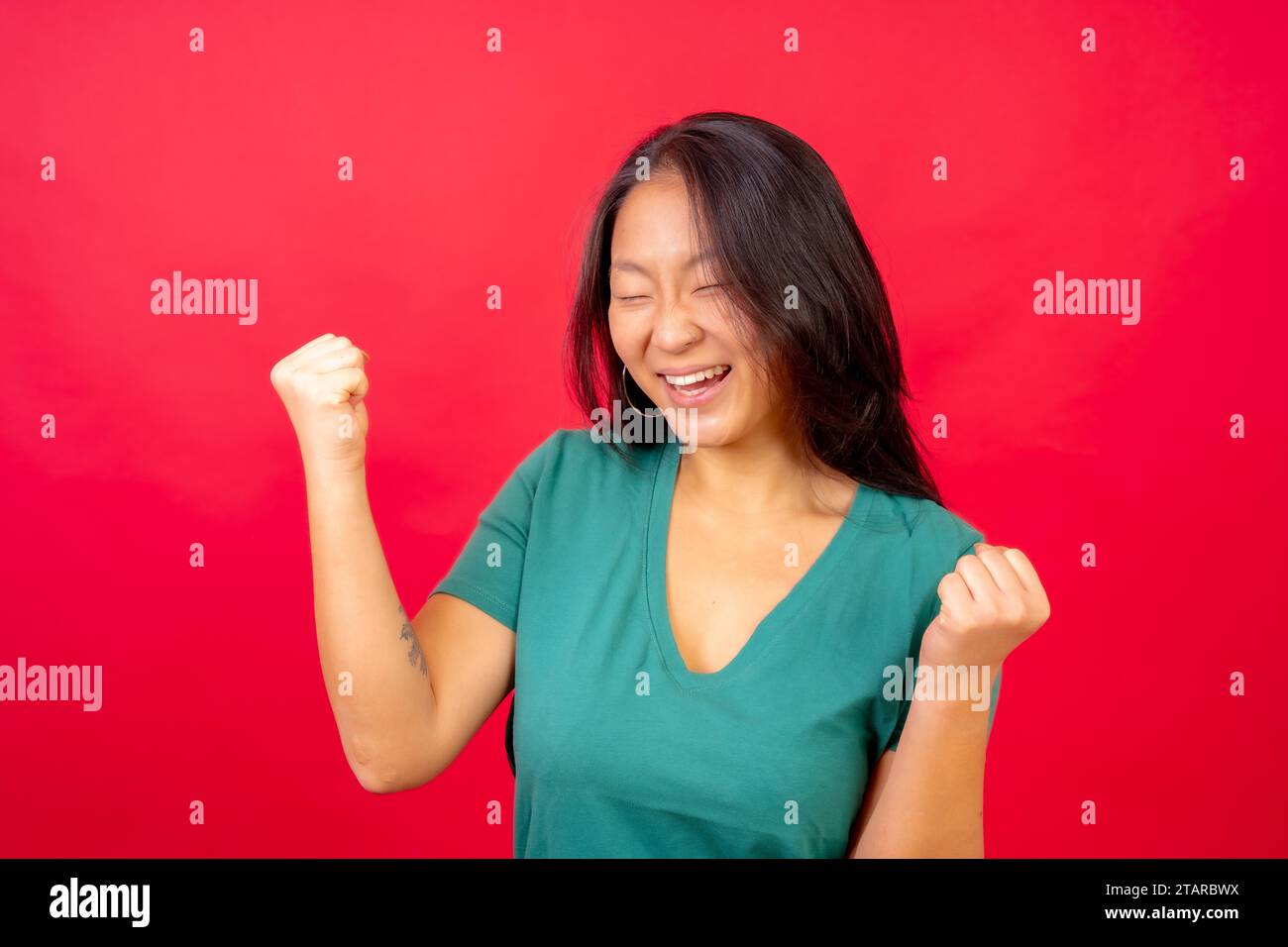 Photo de studio avec fond rouge d'une femme chinoise célébrant lever le poing avec les yeux fermés Banque D'Images