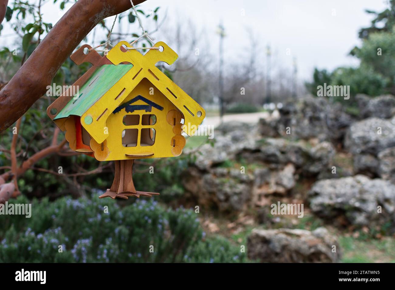 Un mangeoire en bois en gros plan. Une maison d'oiseau en bois jaune vert coloré est accrochée à une branche dans le parc. Arrière-plan flou, faible profondeur de champ. Le Banque D'Images