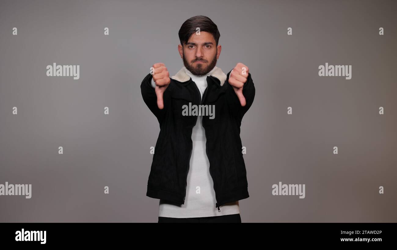 Un jeune homme posant avec un geste pouce vers le bas et exprimant son aversion sur un fond gris. Banque D'Images