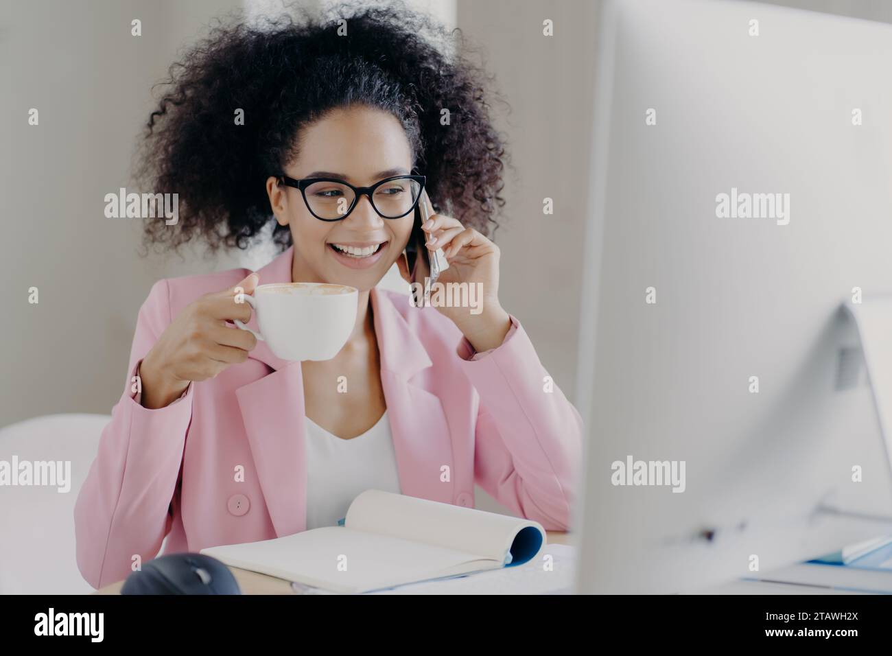 Femme multitâche en blazer rose sur appel téléphonique et profiter du café Banque D'Images