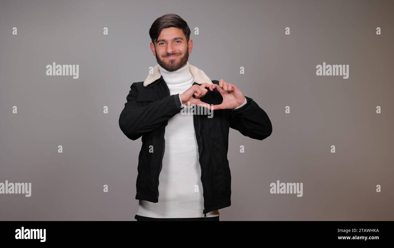 Un jeune homme heureux posant avec un signe d'amour sur un fond gris. Banque D'Images