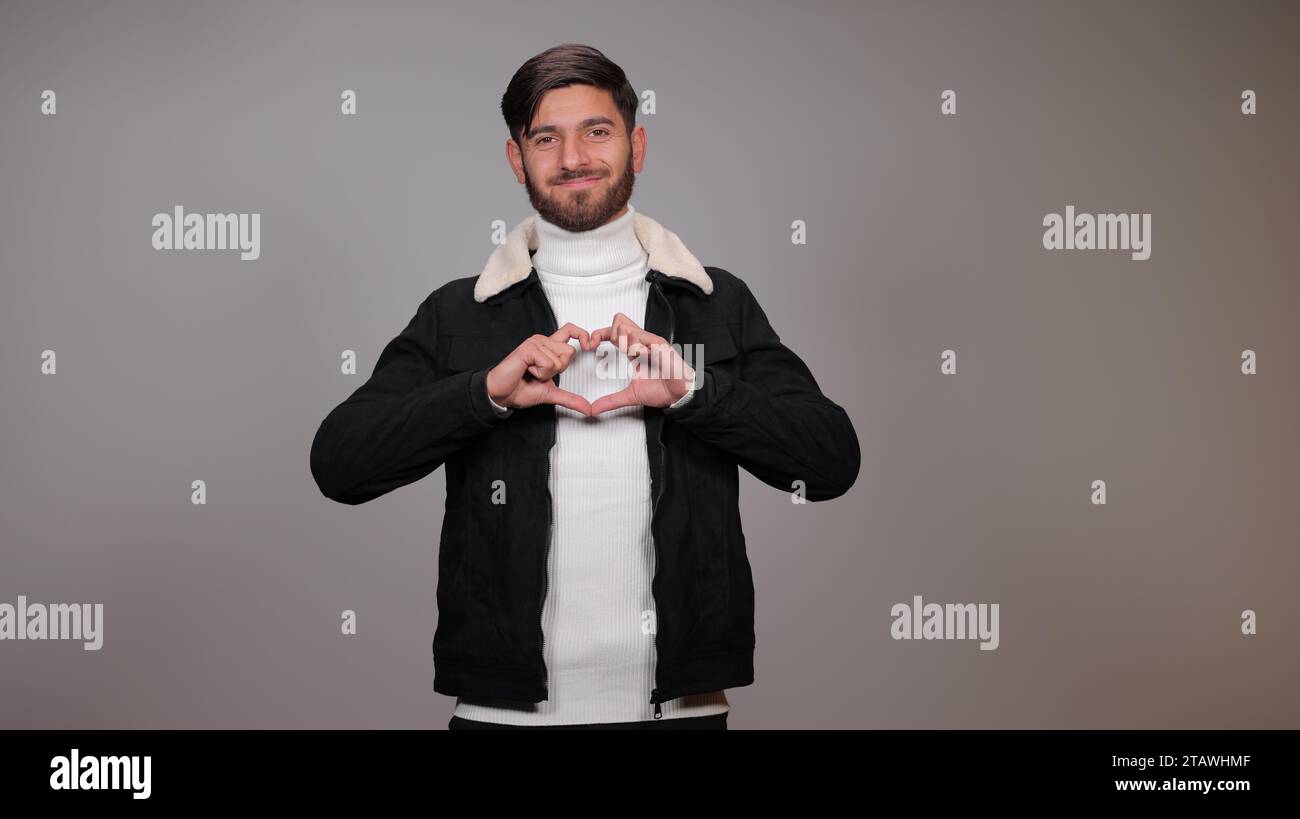 Un jeune homme heureux posant avec un signe d'amour sur un fond gris. Banque D'Images