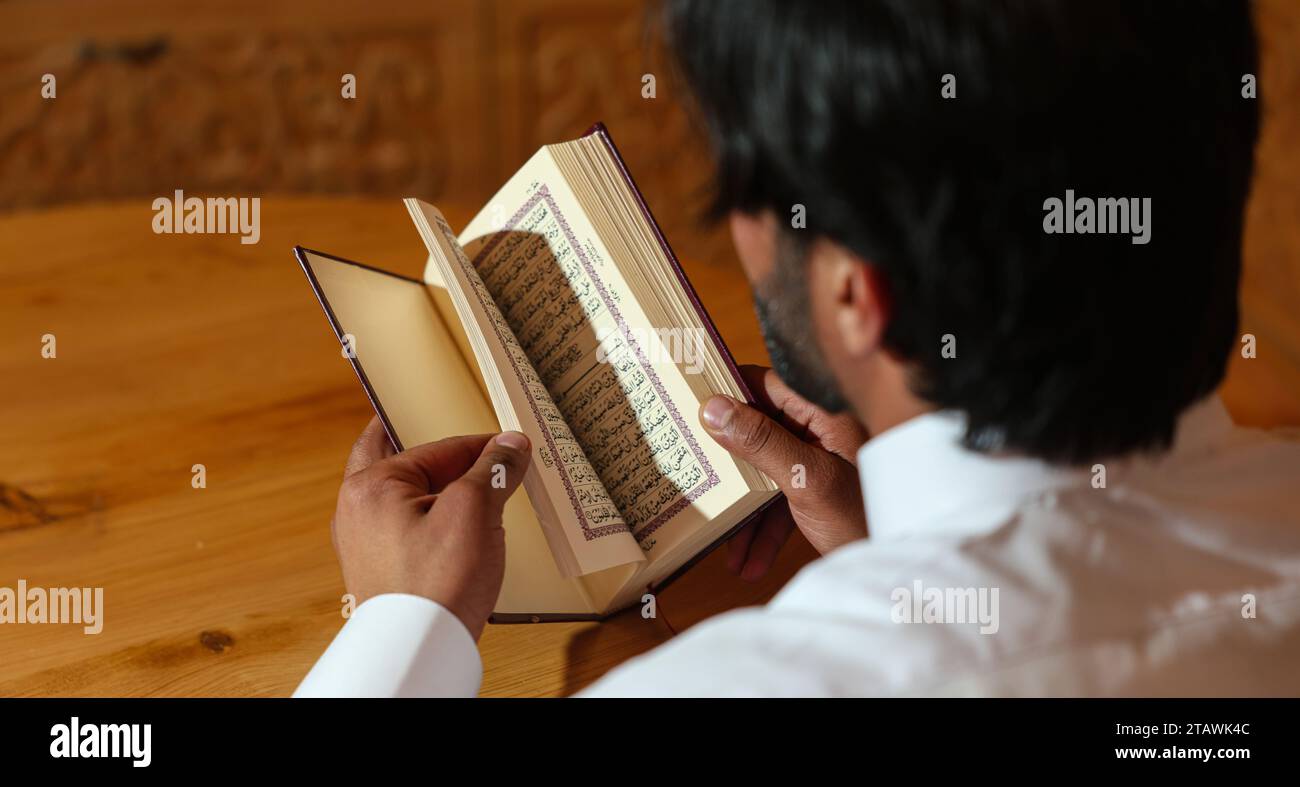Homme musulman lisant le Saint Coran. Saint Coran en main avec texte arabe signifiant Al Coran. Banque D'Images