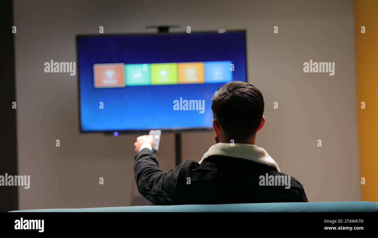 Un jeune homme regardant la télévision et changeant de chaîne avec une télécommande. Banque D'Images