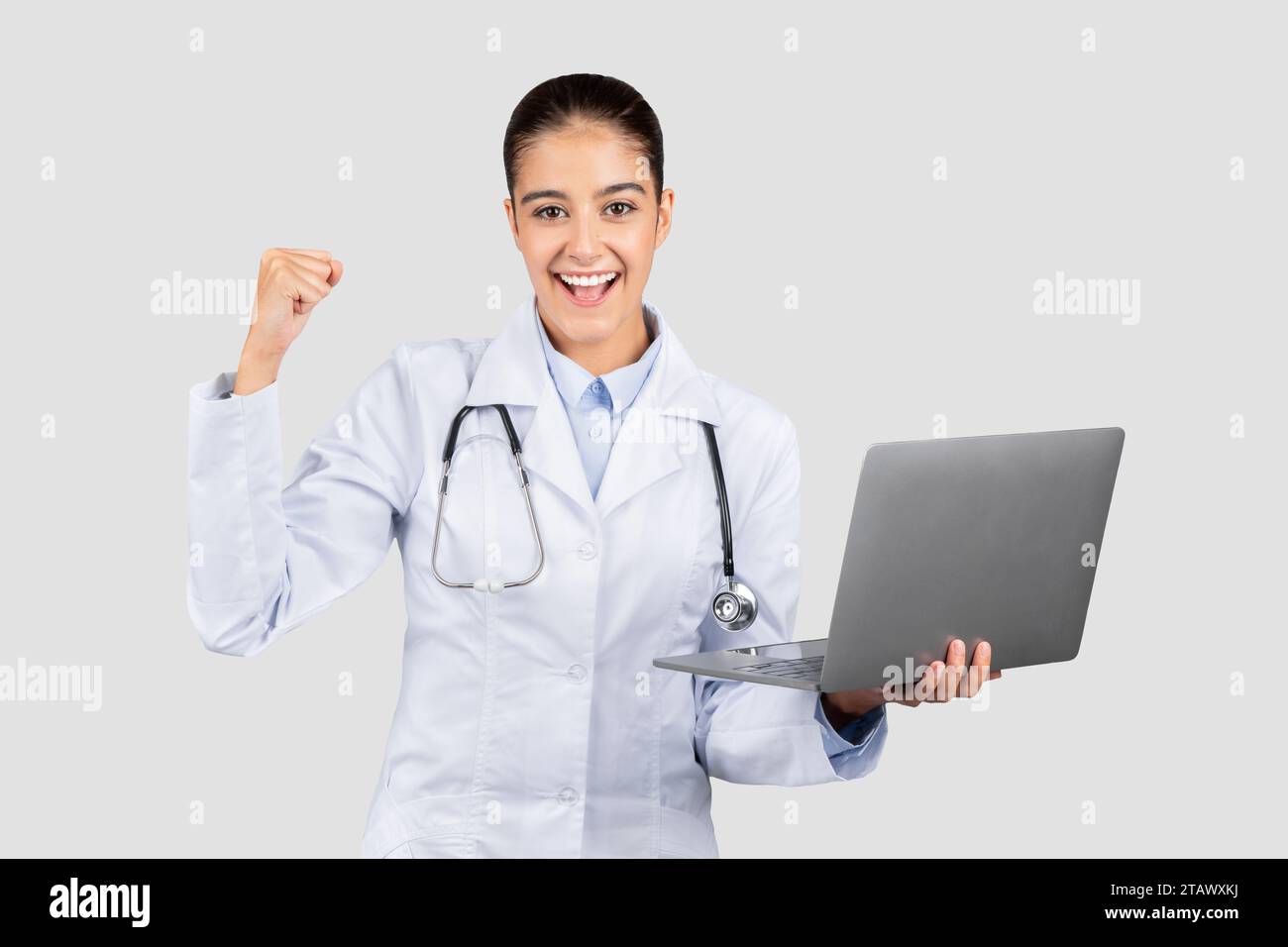 Heureux millennial femme médecin européenne avec ordinateur, célébrer la victoire, le succès avec le poing de hausse dans le manteau blanc Banque D'Images