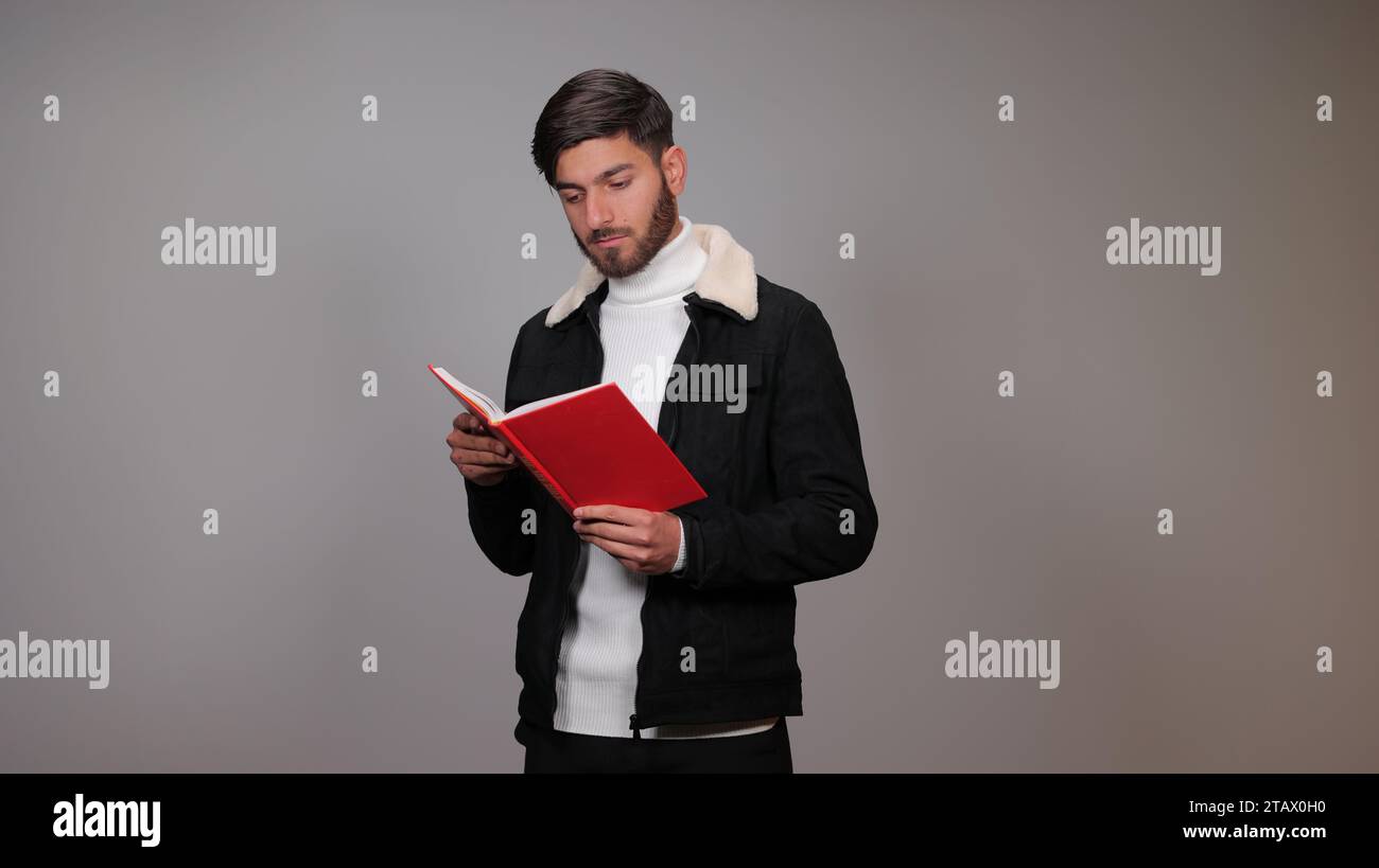 Un jeune homme lisant un livre sur fond gris Banque D'Images