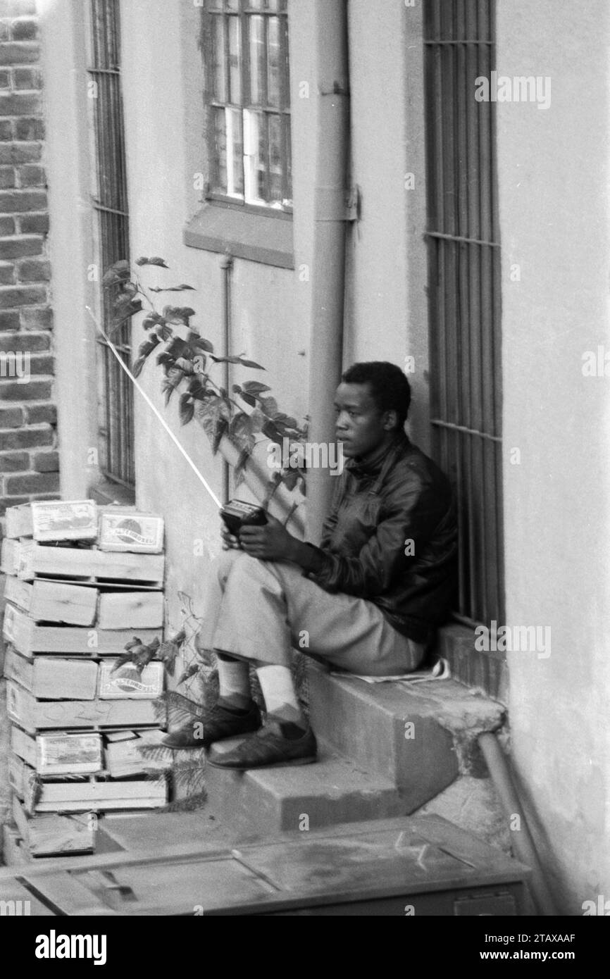 Travailleur de magasin prenant une pause assis sur la marche arrière de magasin écoutant la radio transistor, Johannesburg Gauteng, Afrique du Sud, 1985. De la collection - Afrique du Sud années 1980 - Archives photographiques Don Minnaar Banque D'Images