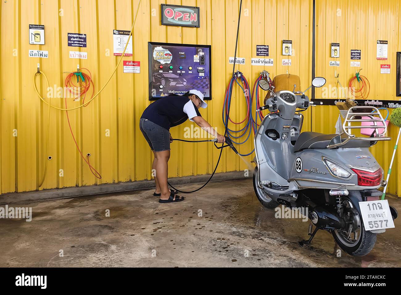 KANCHANABURI, THAÏLANDE-novembre 21,2023 : Femme heureuse non identifiée lavant en libre-service sa moto à la machine automatique de lavage de voiture à pièce de monnaie. A. Banque D'Images