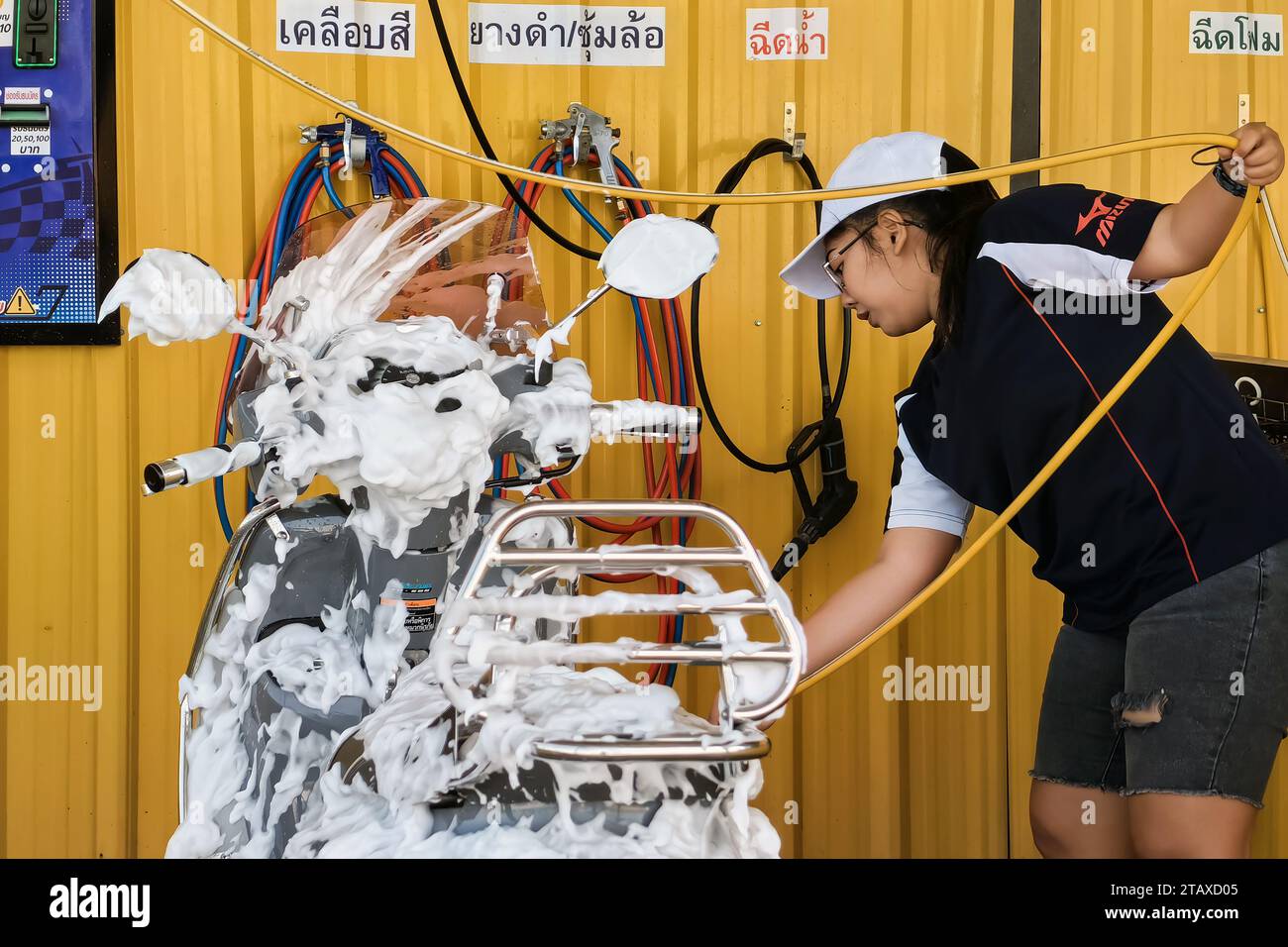KANCHANABURI, THAÏLANDE-novembre 21,2023 : Femme heureuse non identifiée lavant en libre-service sa moto à la machine automatique de lavage de voiture à pièce de monnaie. A. Banque D'Images