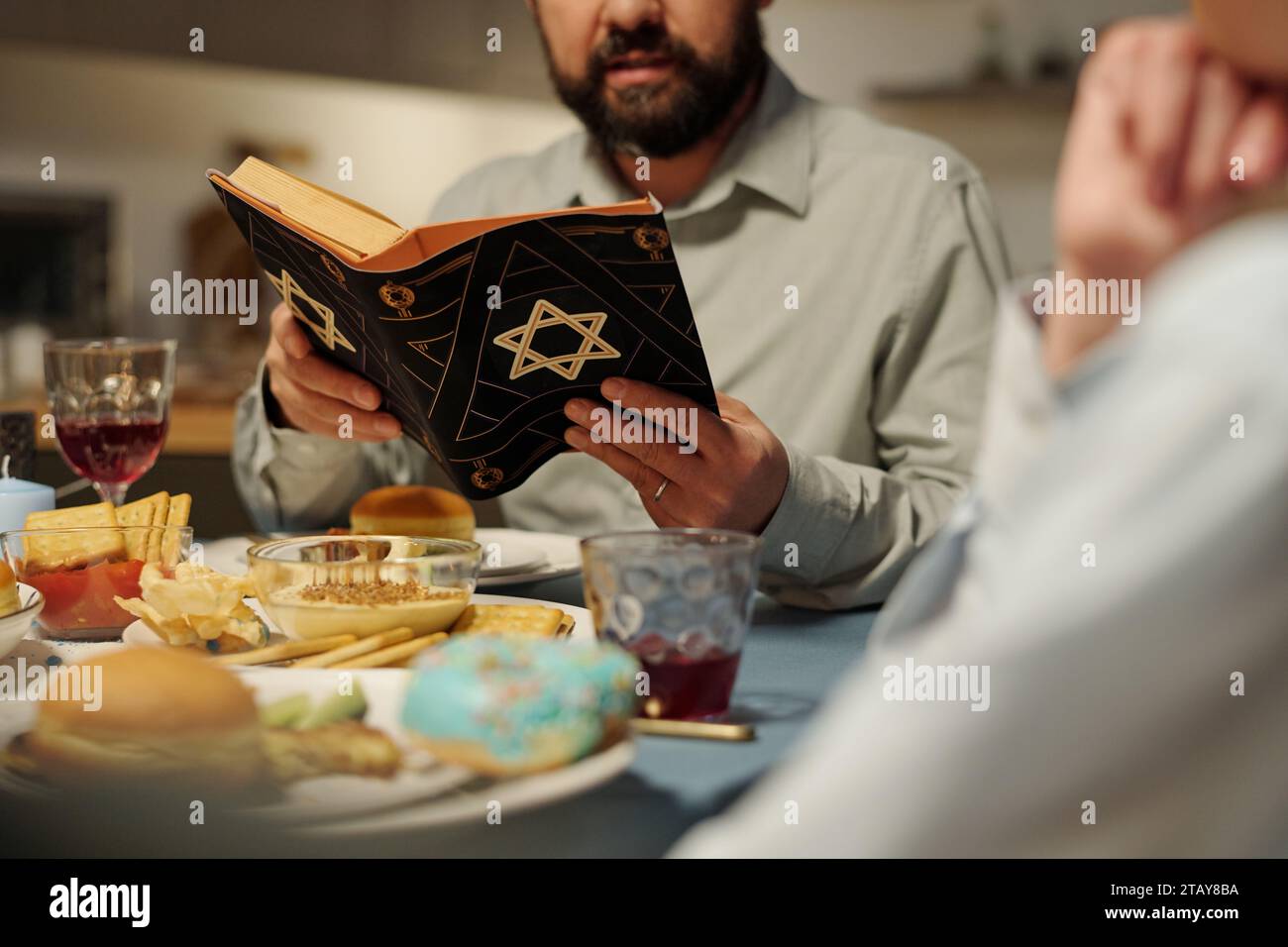 Plan recadré de l'homme barbu avec la Torah ouverte lisant des psaumes ou d'autres versets de l'ancien Testament assis près de la table servie Banque D'Images