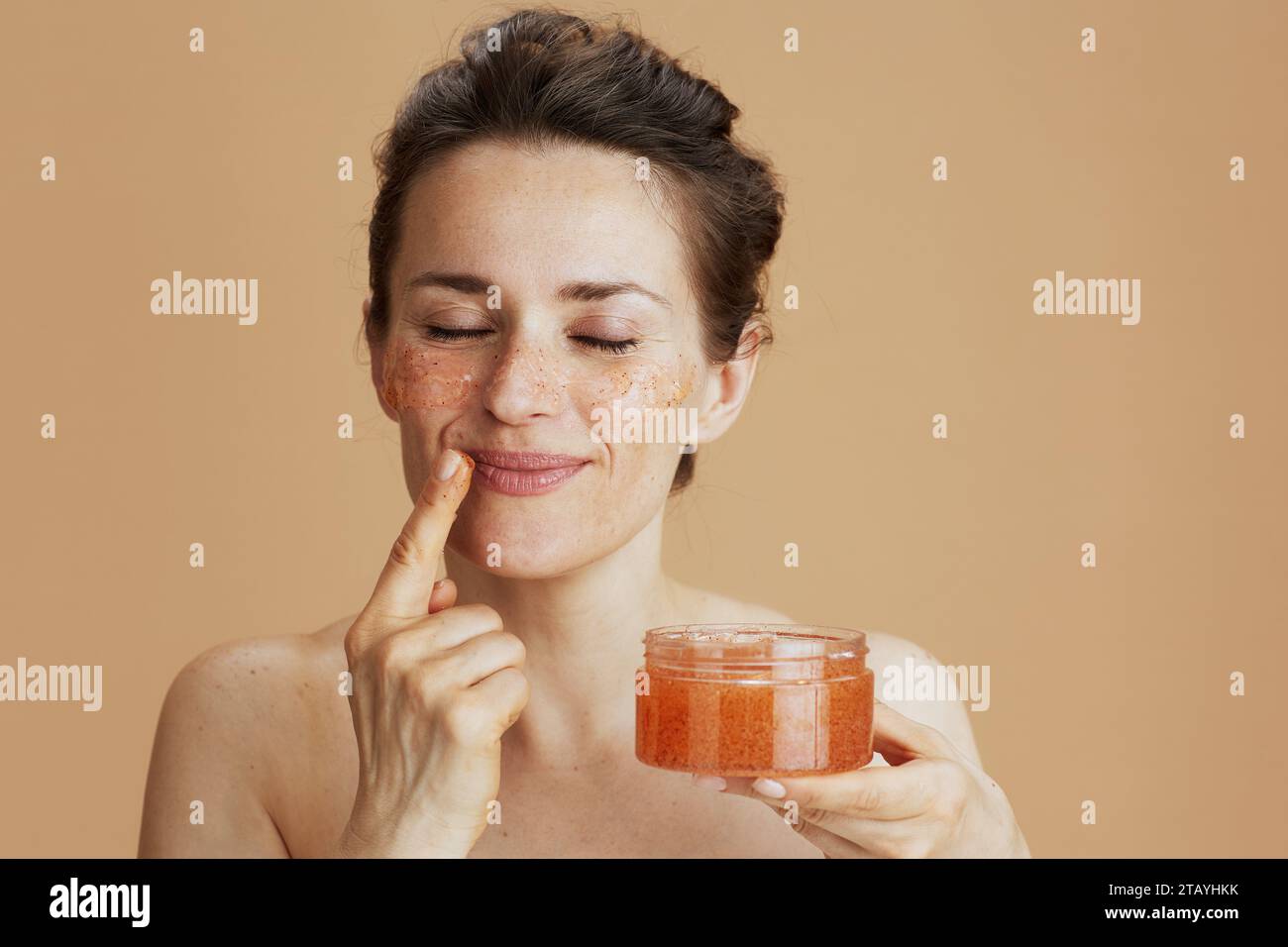 femme moderne détendue avec gommage du visage isolé sur beige. Banque D'Images