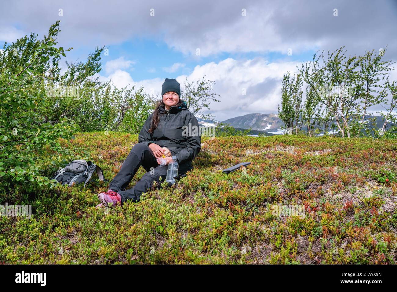 Femme mûre prend pause de repos, profitant du soleil rare de montagne, tenant la bouteille d'eau et des sandwichs dans le paquet en plastique, la randonnée haute dans les montagnes norvégiennes. Lui Banque D'Images