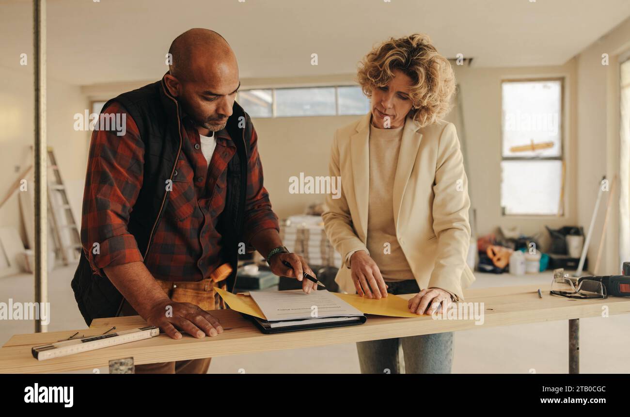 Entrepreneur mature et femme propriétaire signant un contrat à l'intérieur pour un projet de rénovation domiciliaire. Ils font preuve de professionnalisme et de dévouement envers Th Banque D'Images