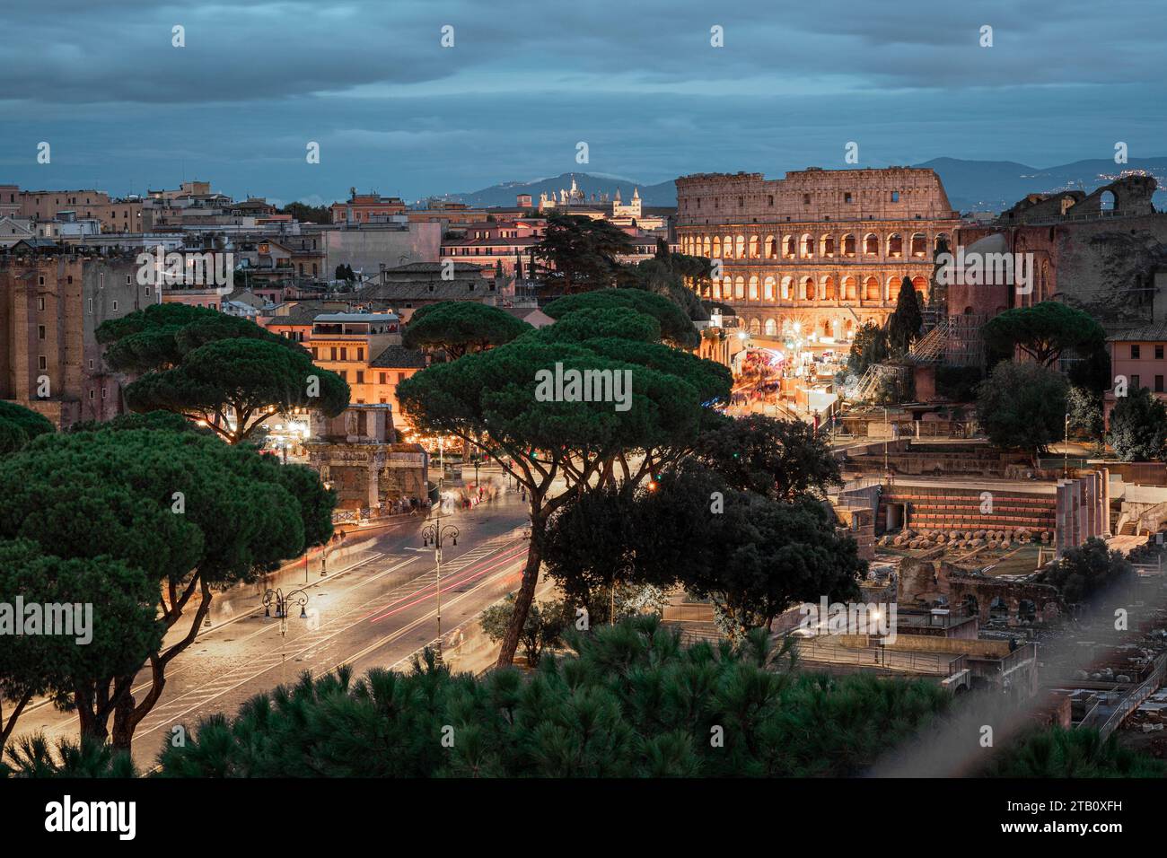 Vue du soir sur le célèbre colisée de rome, vu de loin. Route visible et arbres menant au célèbre amphithéâtre, d'autres maisons et ruines visibles arou Banque D'Images