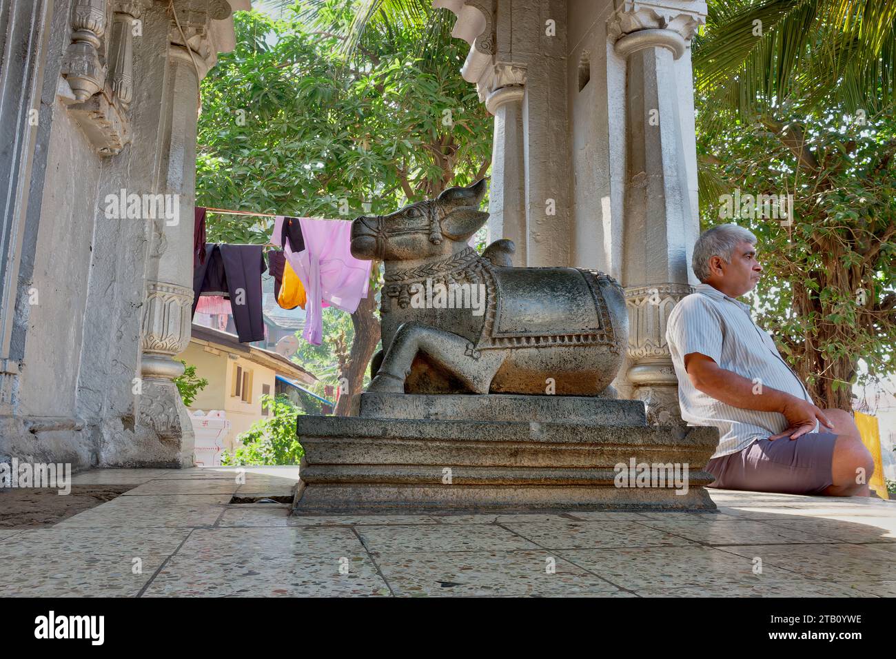 Un homme est assis à côté de la figure d'un taureau Nandi, le véhicule de dieu Shiva, dans un petit temple Shiva à Banganga Tank, Walkeshwar, Mumbai, Inde Banque D'Images