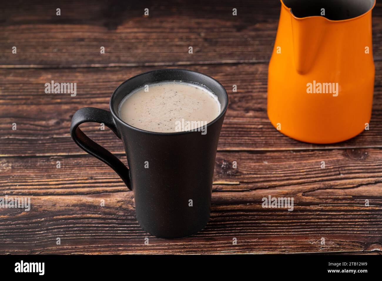 Lait avec café turc dans une tasse noire sur une table en bois Banque D'Images