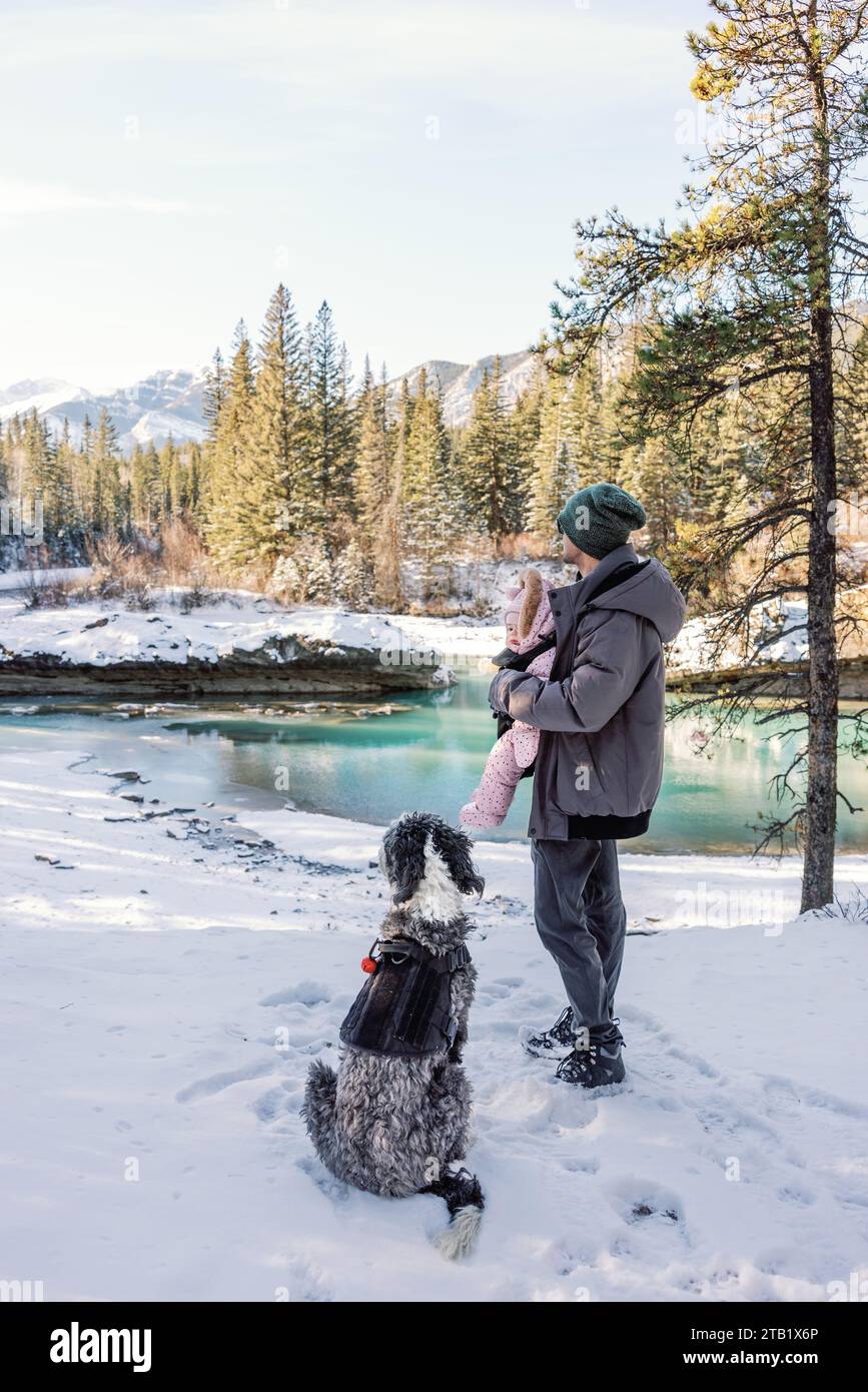 Père actif avec bébé et chien en randonnée hivernale le long de la rivière de montagne Banque D'Images