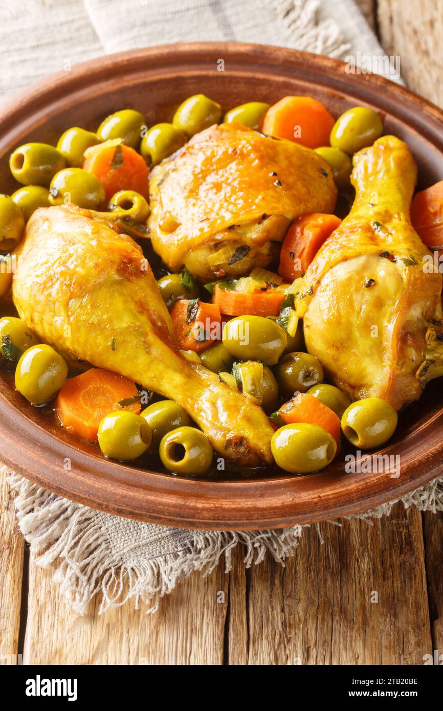 Plat traditionnel algérien Tajine Zitoune de poulet, carottes et olives vertes gros plan sur table en bois. Vertical Banque D'Images