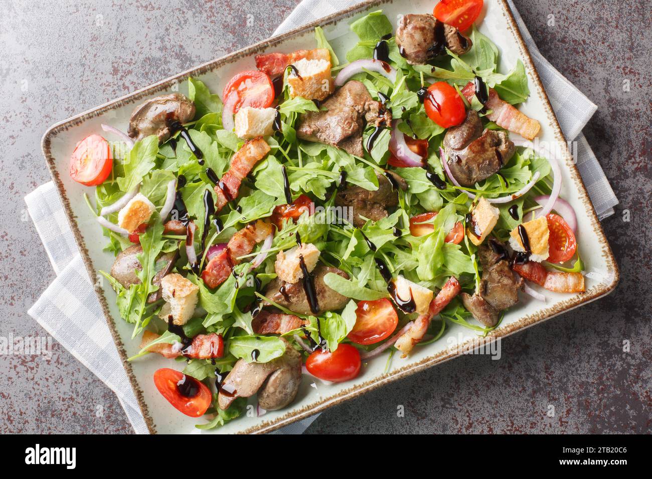 Délicieuse salade diététique de foie de poulet, roquette, oignons, tomates, croûtons et bacon gros plan dans une assiette sur la table. Vue de dessus horizontale depuis abo Banque D'Images