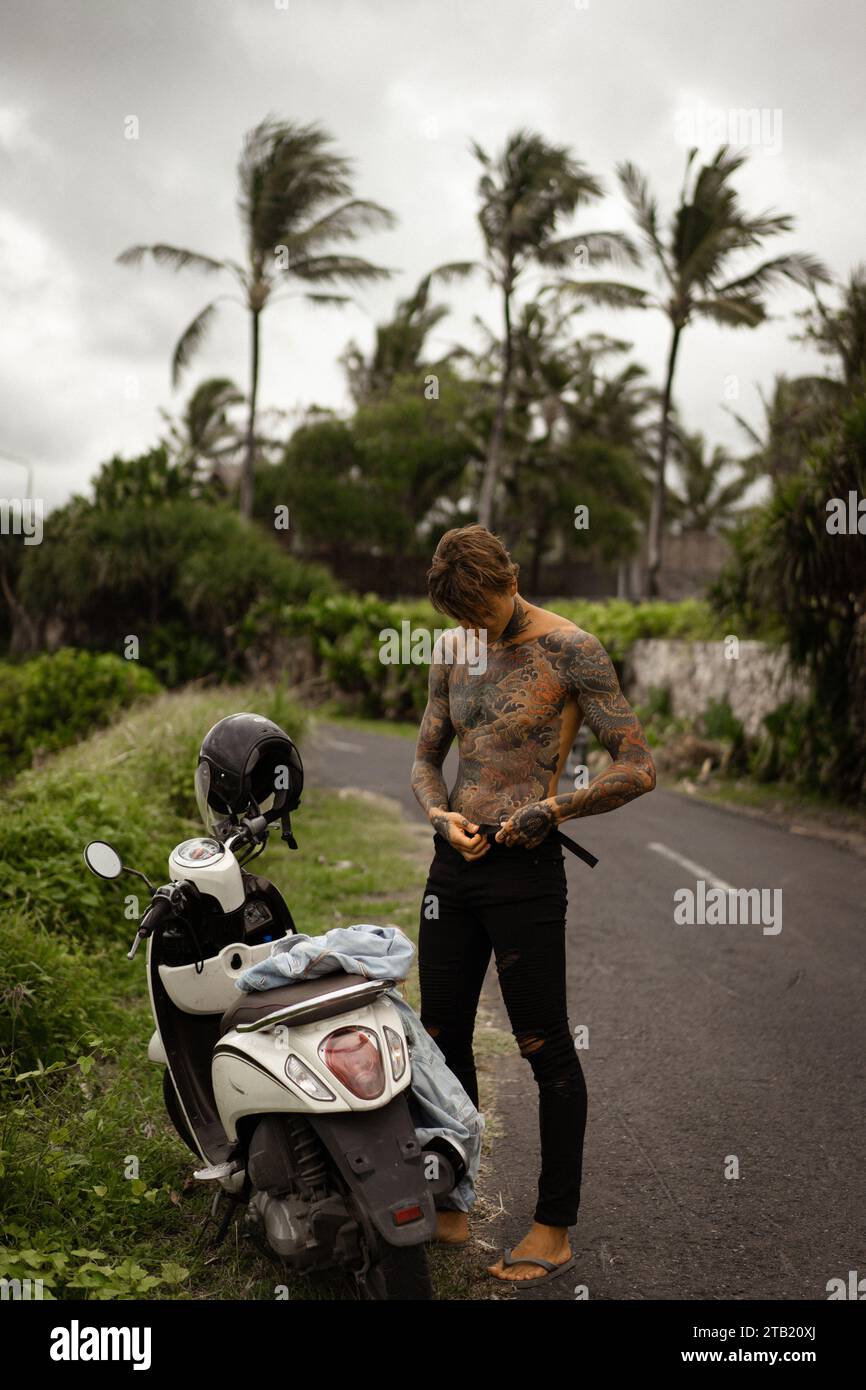 Jeune homme tatoué près d'une moto sur une île tropicale. Vacances Bali Banque D'Images