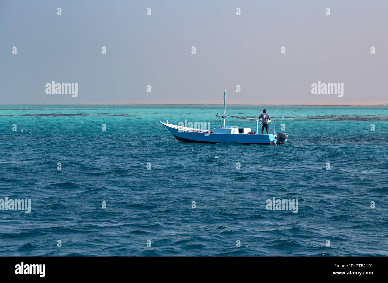 Pêcheur sur un petit bateau bleu, naviguant dans les eaux bleues claires Banque D'Images